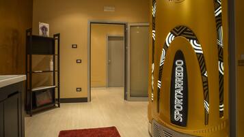 A hotel corridor with a red carpet, a vending machine labeled "SPORTAREDO", and a door leading to another room.