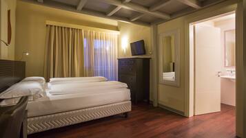 Habitación de hotel con cama, escritorio, cómoda, televisor y baño visible a través de una puerta abierta.