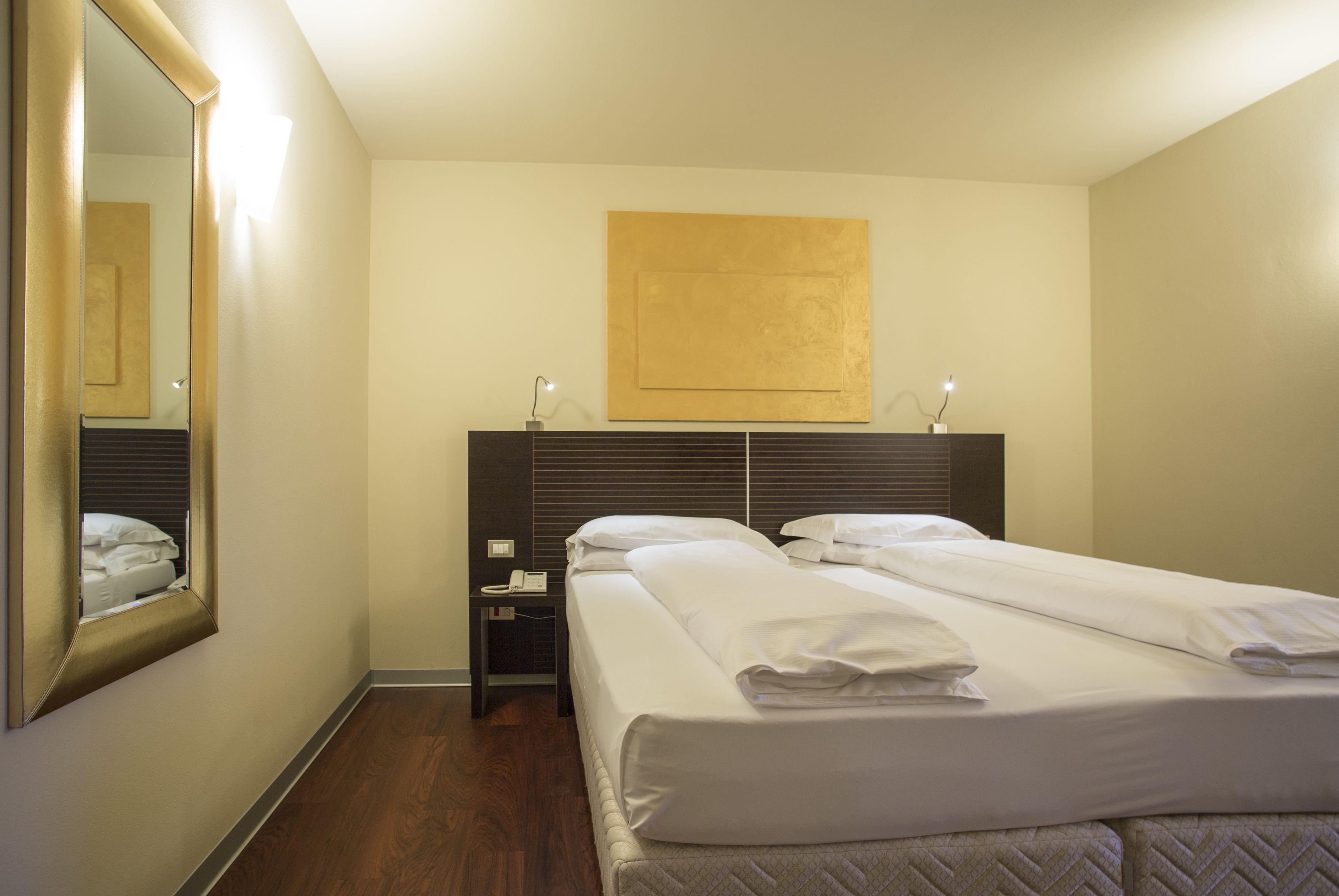 Une chambre d’hôtel avec un grand lit, une table de chevet avec une lampe, un miroir et une œuvre d’art accrochée au mur.