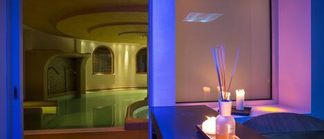 A spa room with a glass-enclosed hot tub, a wooden reception desk with candles, and a window with a view of the hot tub.