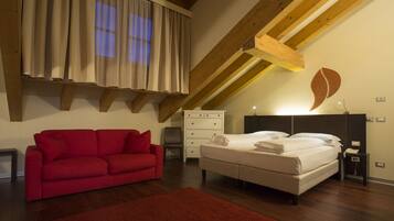 Un dormitorio con cama, sofá rojo, cómoda y techo de madera.