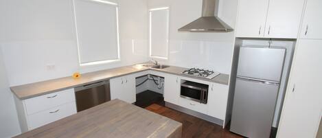 A modern kitchen with white cabinets, a stainless steel refrigerator, a built-in oven, and a wooden countertop.