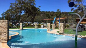 A swimming pool with a water feature, surrounded by stone pillars and a playground area. - NRMA Ocean Beach Holiday Resort (Umina Beach)