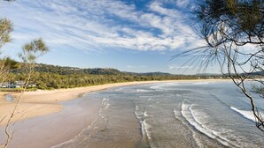 A beach with clear skies, gentle waves, and a forested hillside in the background. - NRMA Ocean Beach Holiday Resort (Umina Beach)