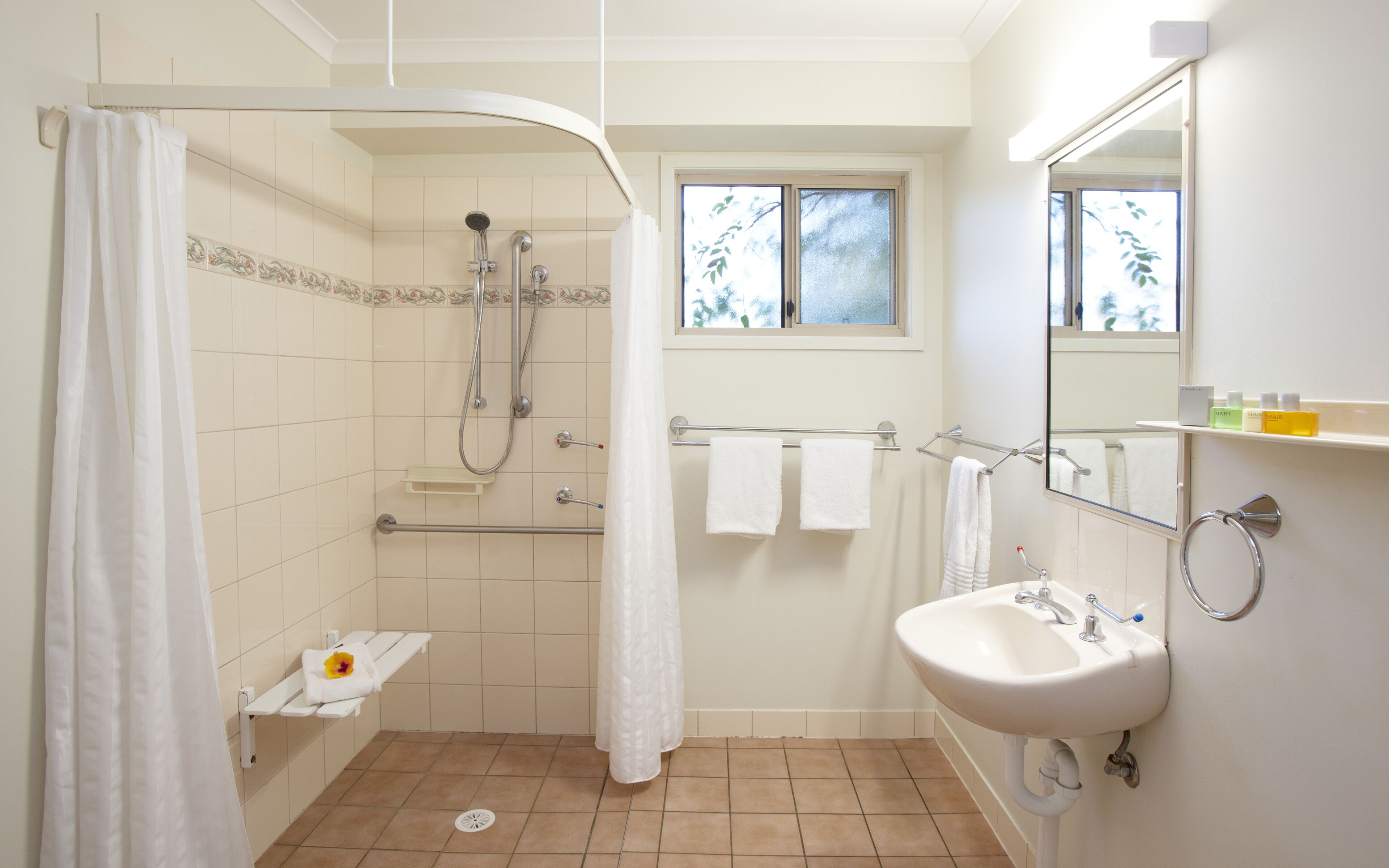A bathroom with a shower, a sink, a window, and a towel rack.