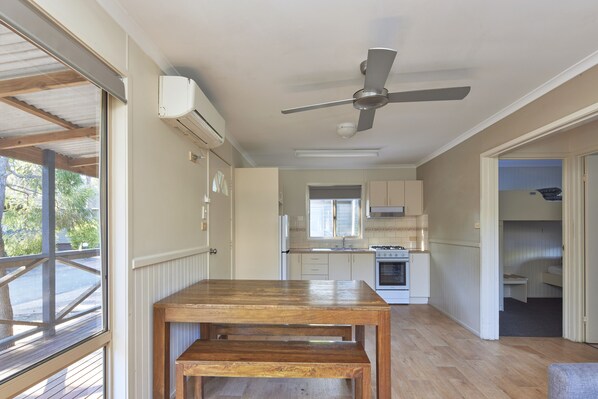 Una cocina amplia con mesa y banco, ventilador de techo y vista al exterior.