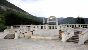 A stone staircase leading to a fountain, surrounded by a balustrade and set against a mountainous backdrop.