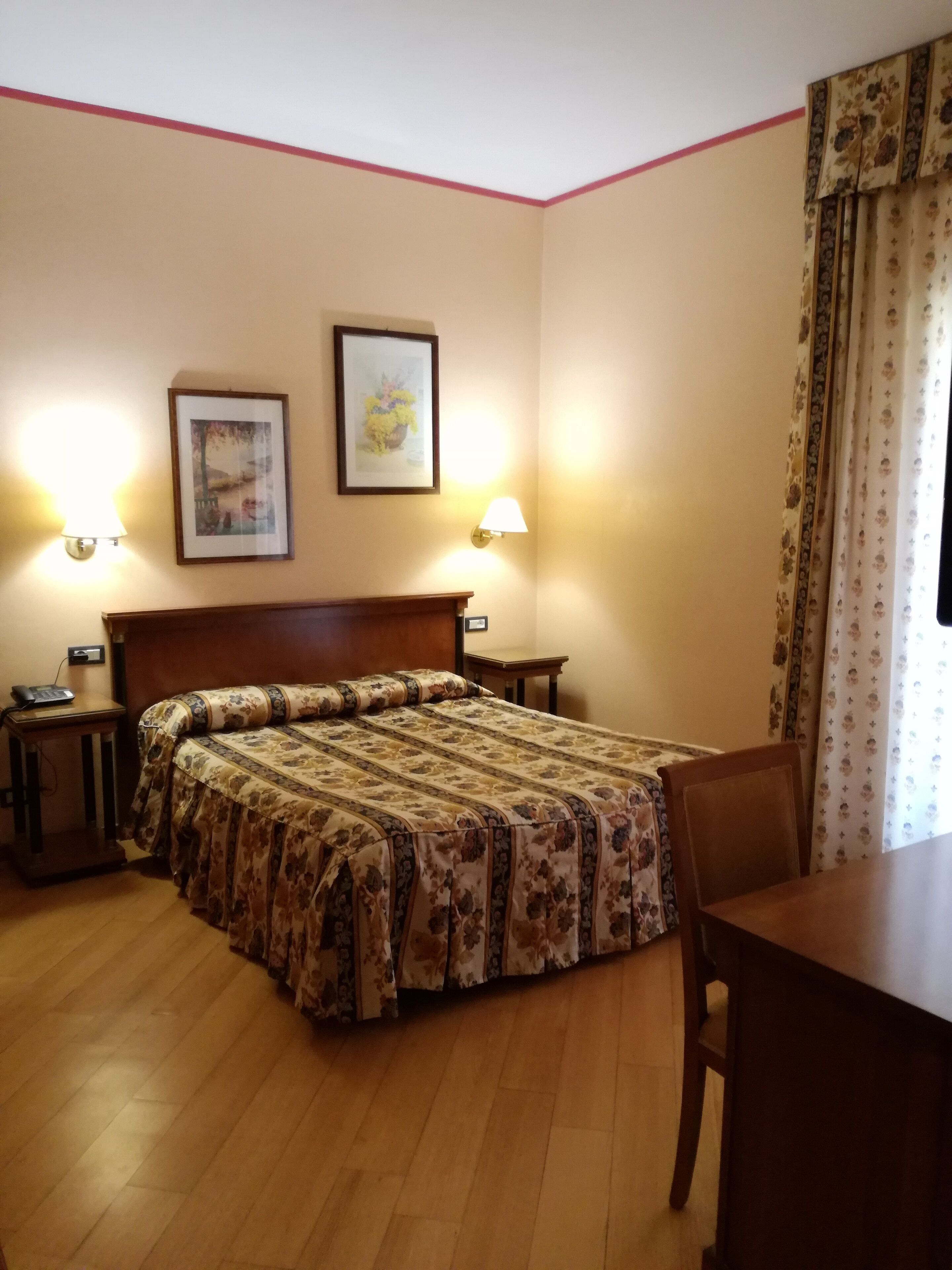 A hotel room with a bed, bedside tables, a desk, and two wall-mounted lamps.