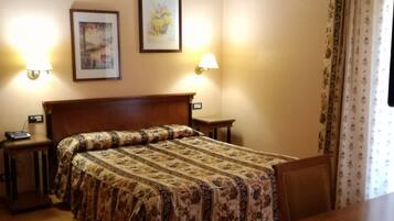 A hotel room with a bed, bedside tables, a desk, and two wall-mounted lamps.
