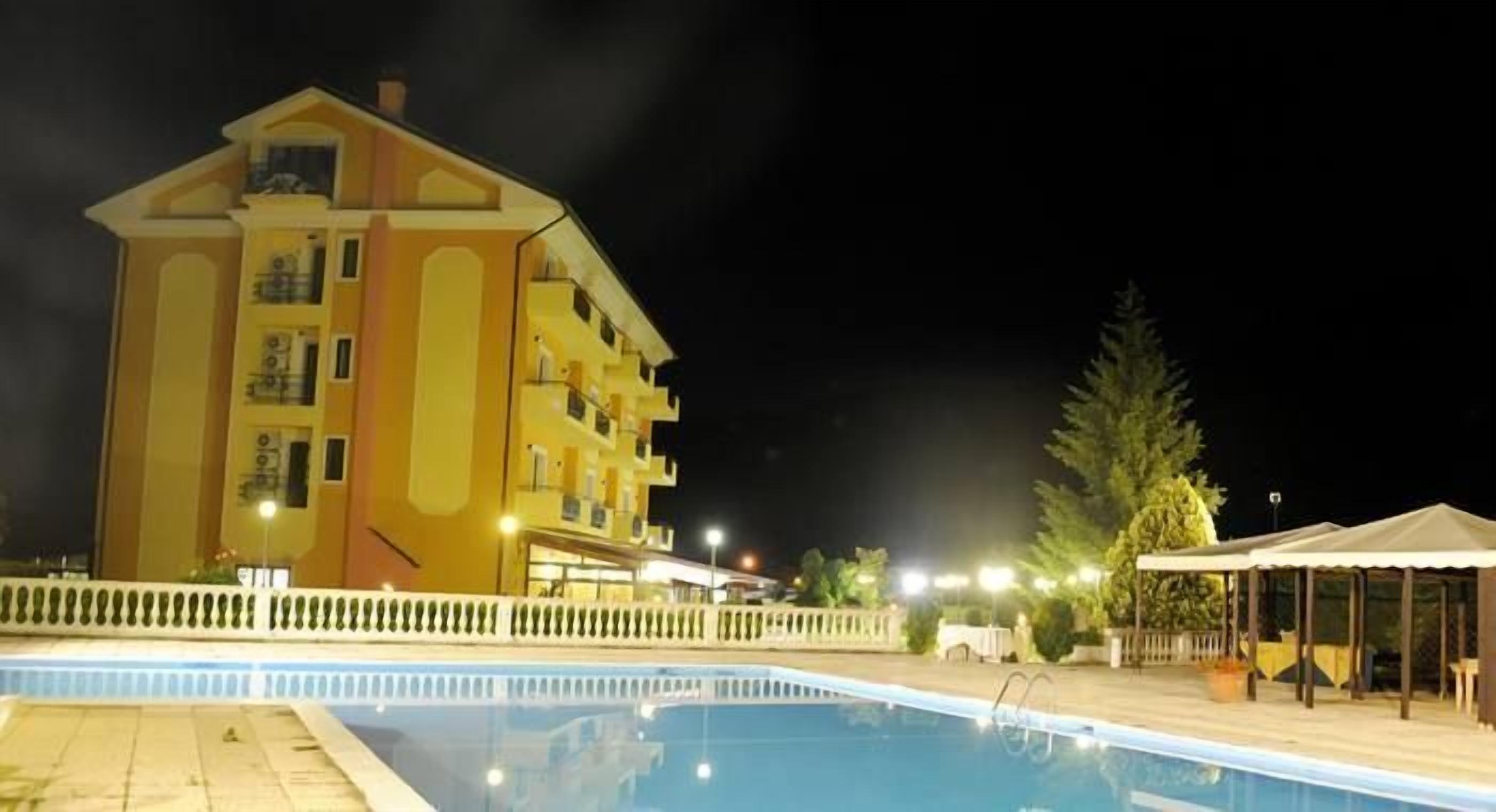 Un hotel con piscina, un espacio exterior cubierto y un edificio grande con varios pisos y balcones.
