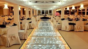 A banquet hall with rows of tables and chairs, a central aisle, and decorative lighting.
