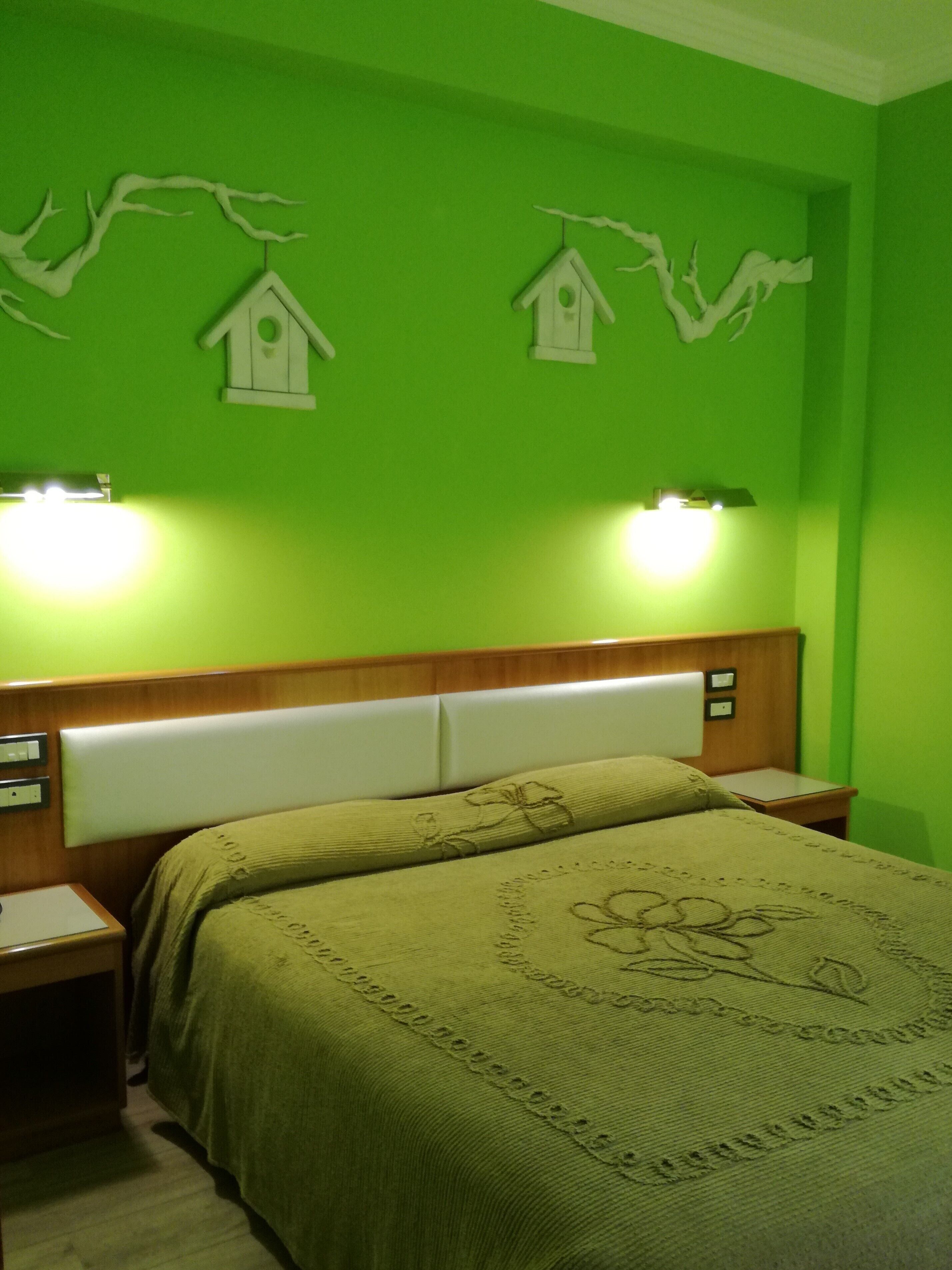 A room with green walls, a wooden headboard, two bedside tables, and a bed with a green bedspread.