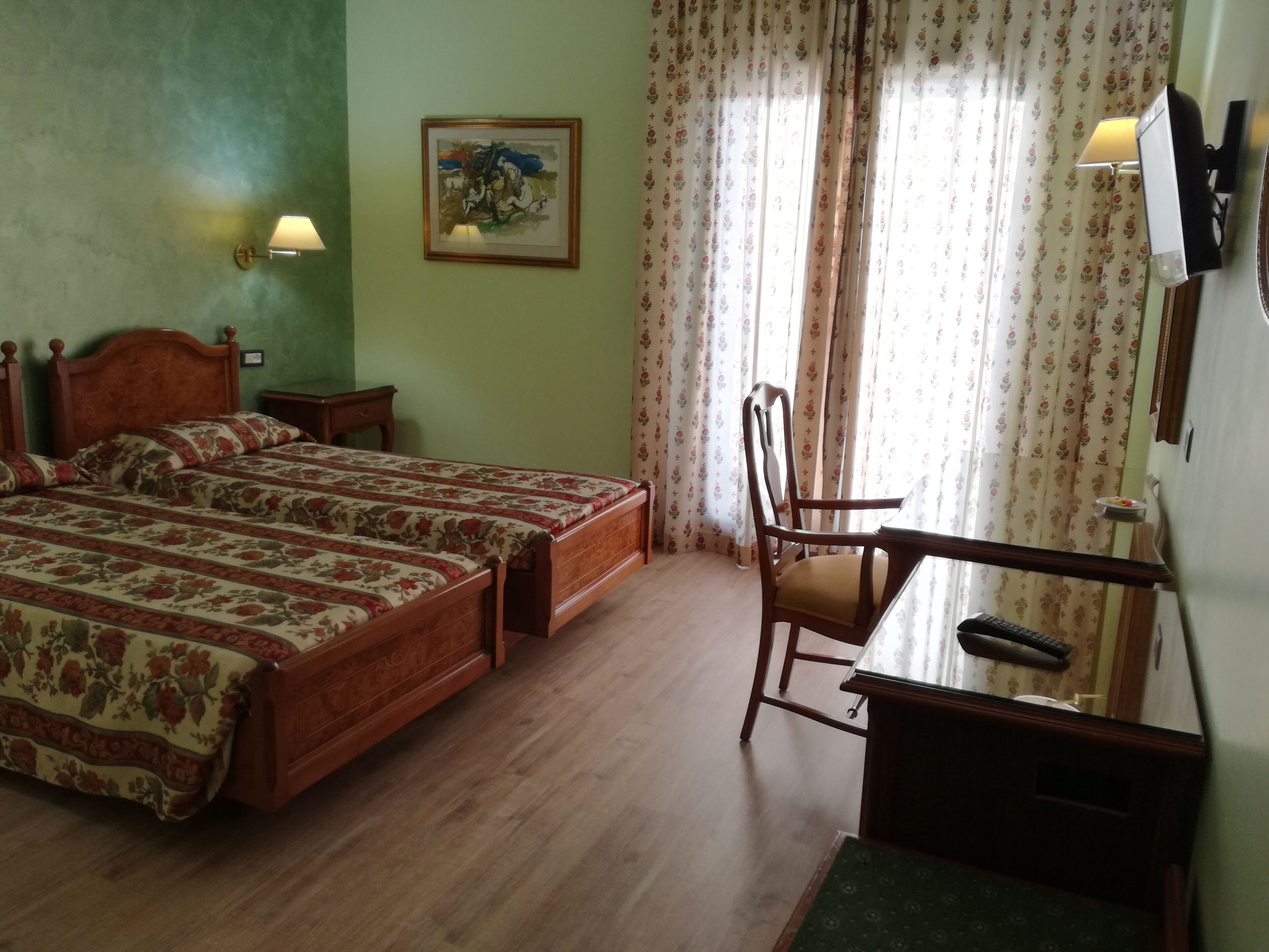 A bedroom with two wooden beds, a desk with a chair, a wall-mounted TV, and a painting on the wall.