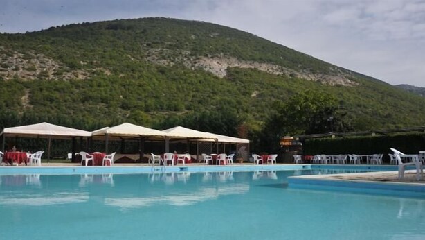 A swimming pool with white lounge chairs and umbrellas, surrounded by a mountainous landscape.