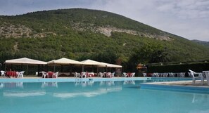 A swimming pool with white lounge chairs and umbrellas, surrounded by a mountainous landscape. - Filippone Hotel & Ristorante (Gioia dei Marsi)