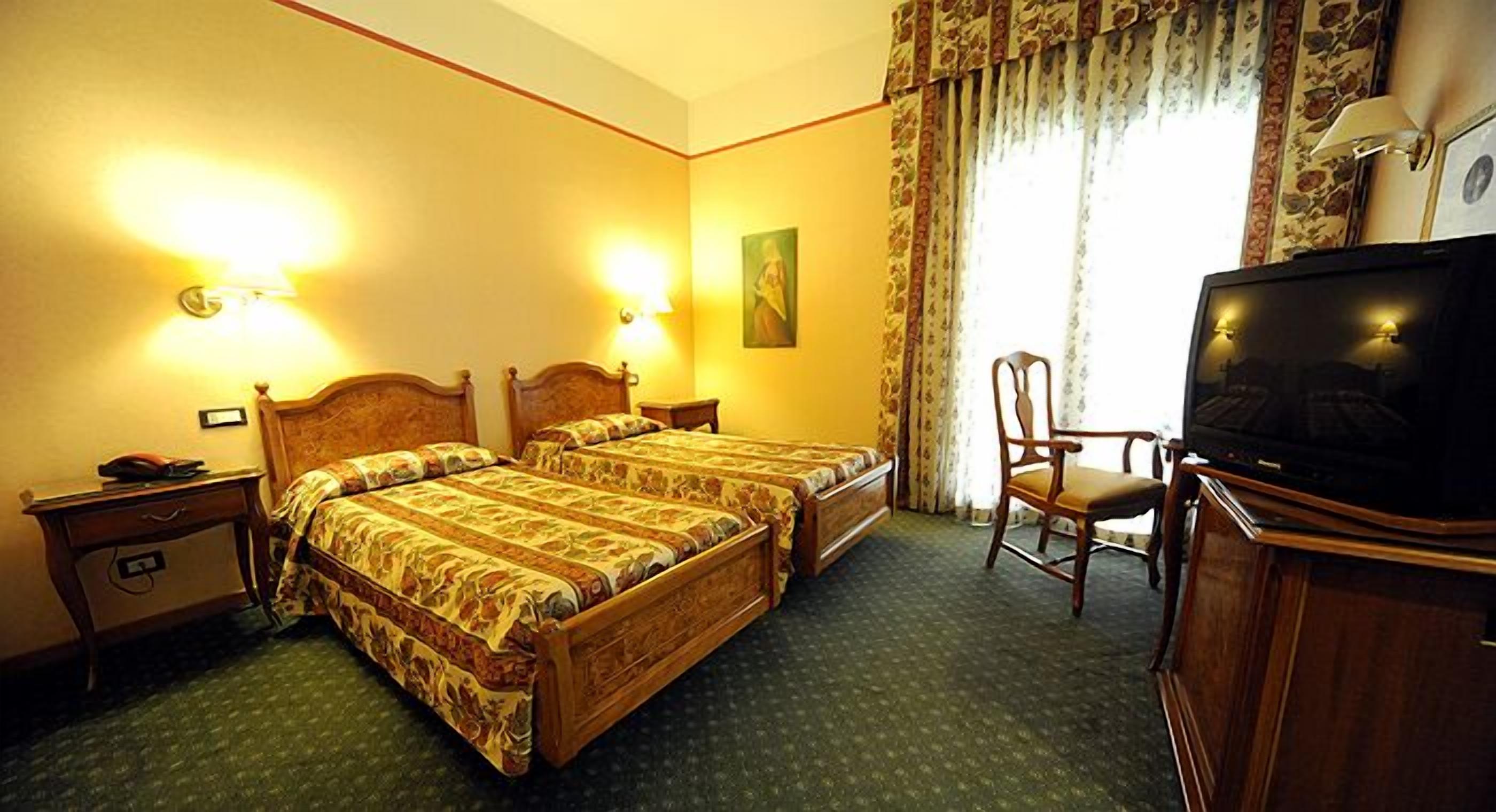 Ein Hotelzimmer mit zwei Holzbetten, einem Fernseher, einem Schreibtisch mit Stuhl und einem Bild an der Wand.