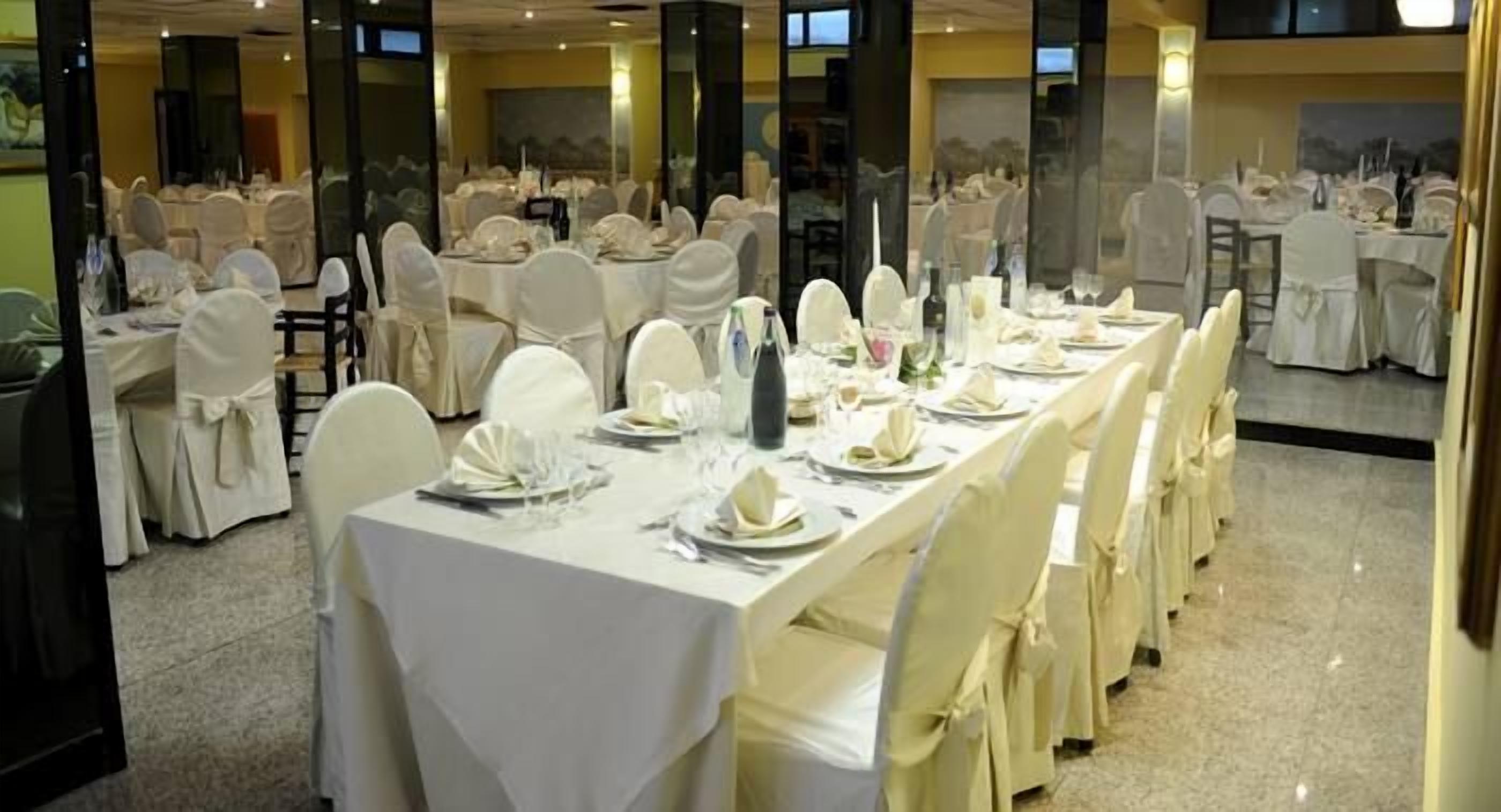 A banquet hall with long tables set for a formal event, featuring white tablecloths and chairs with white covers.