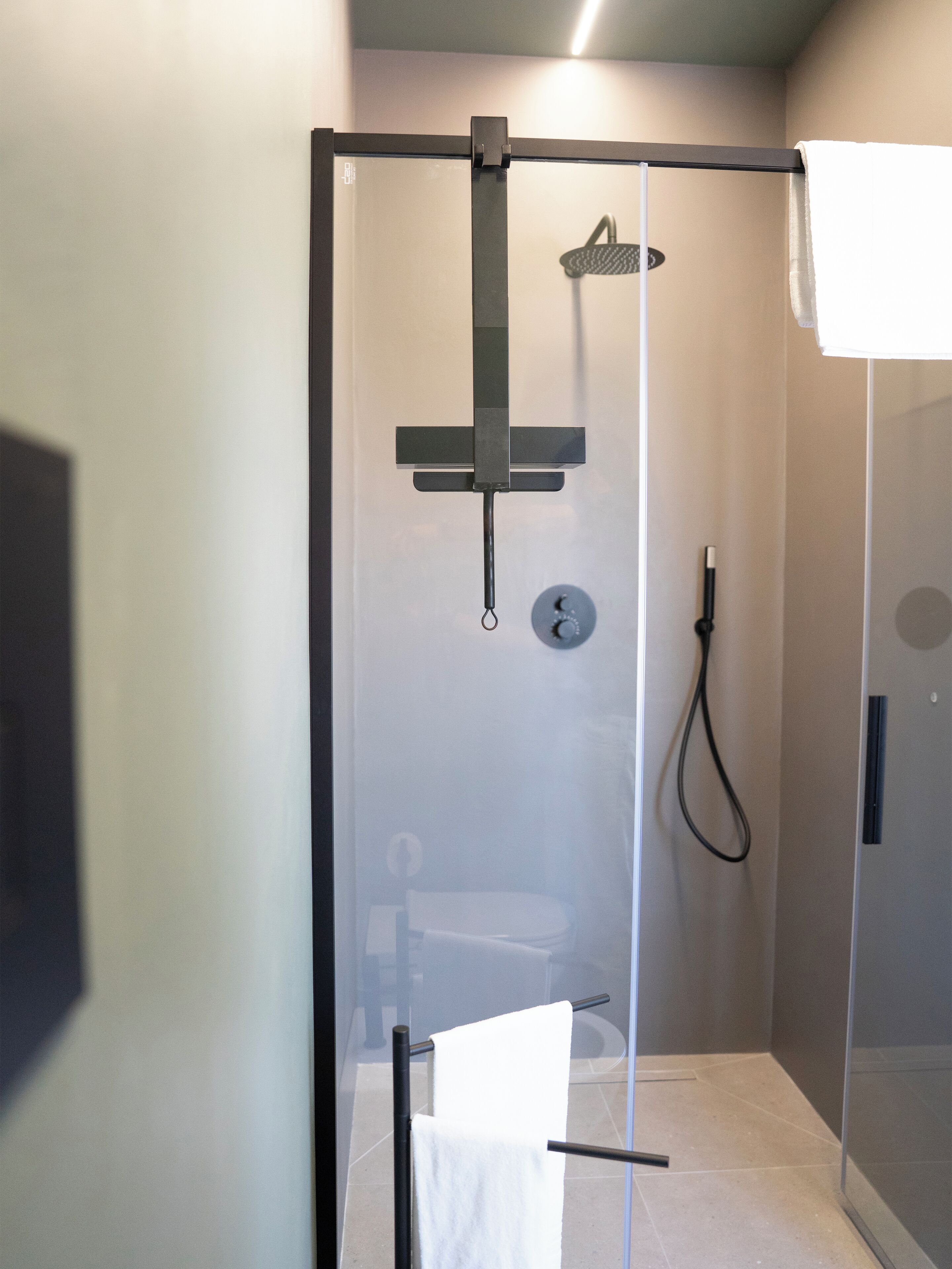 A glass-enclosed shower with a handheld showerhead and a wall-mounted faucet.