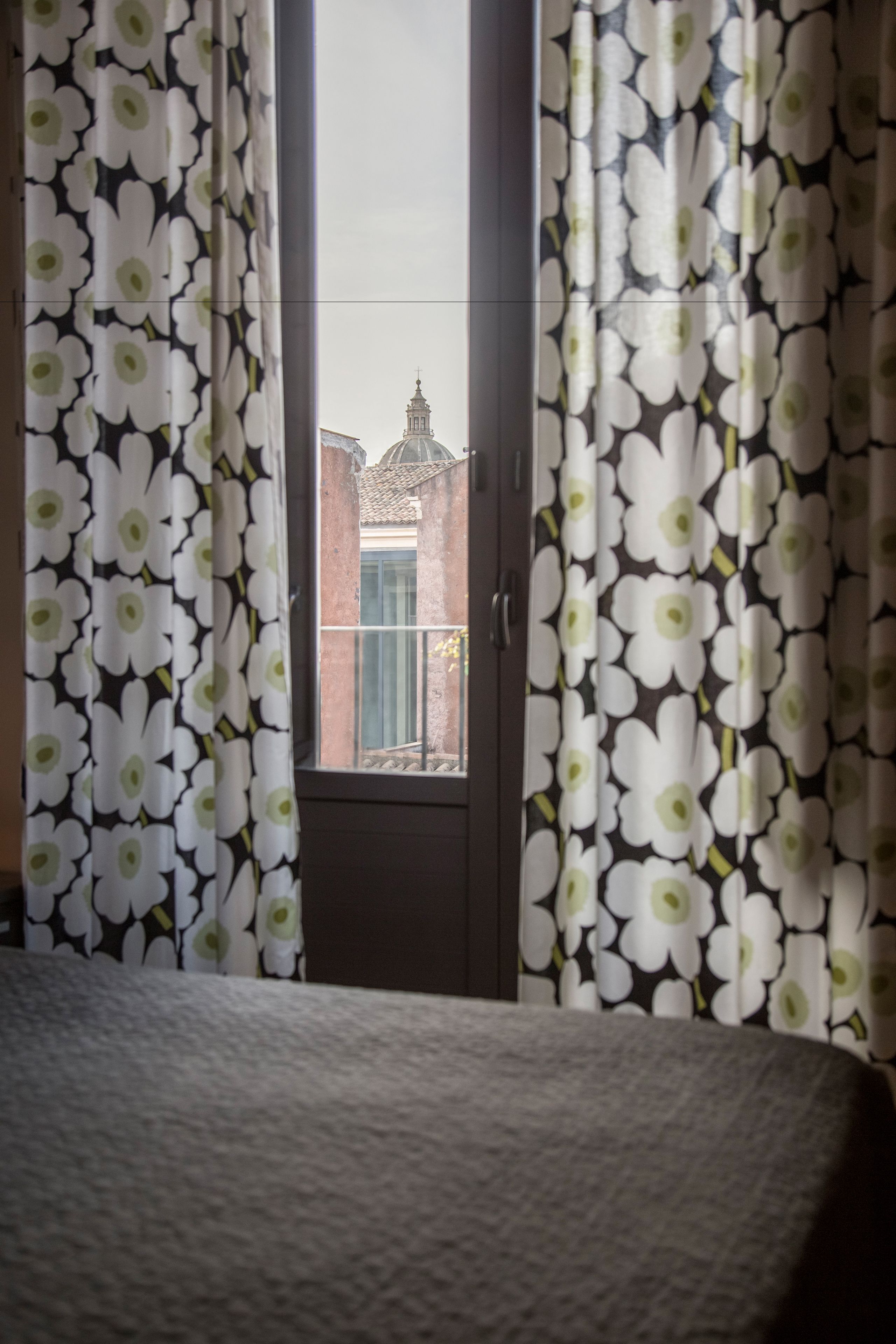 A room with a bed, a window with curtains, and a view of a building with a dome.
