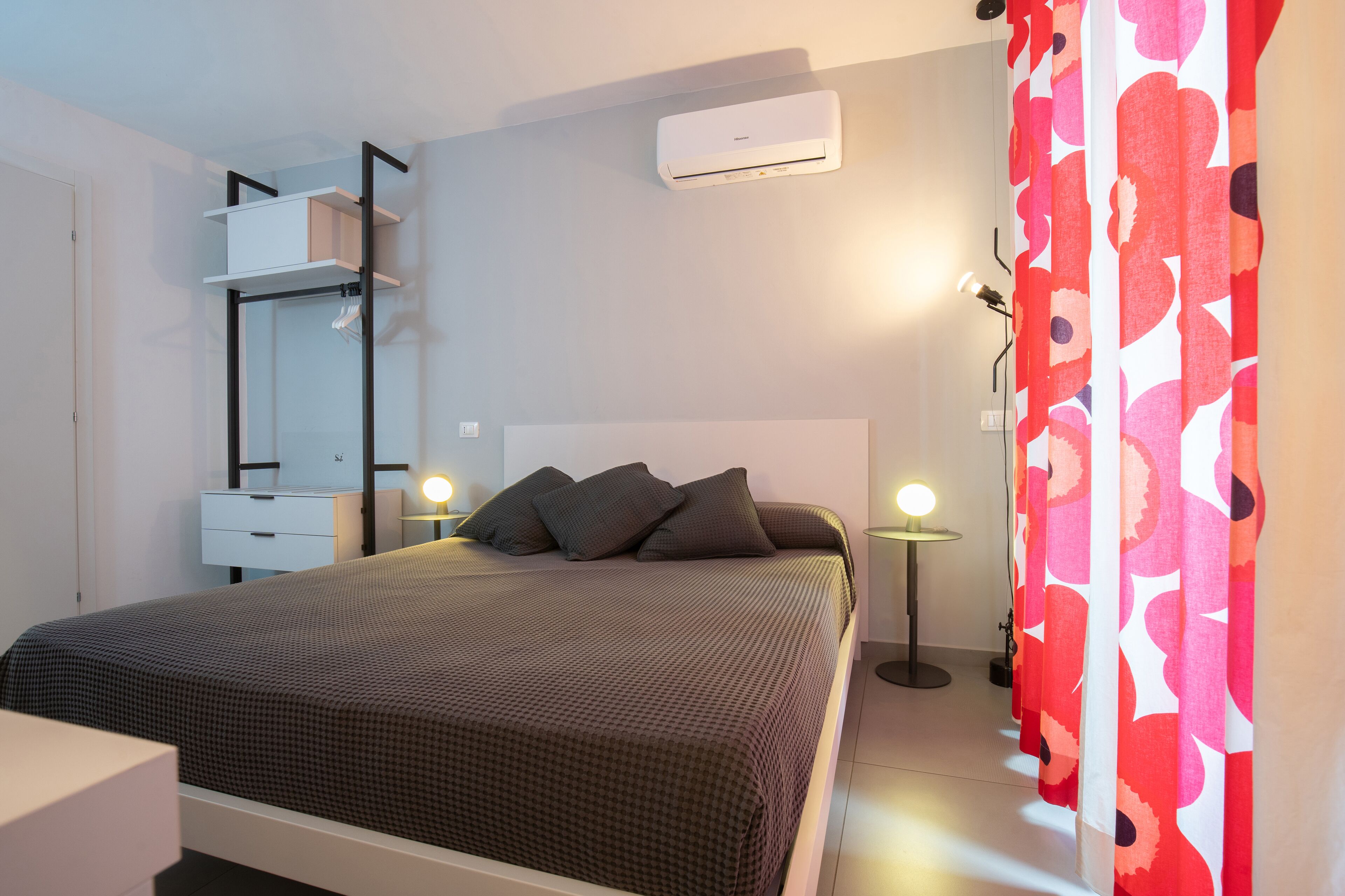 A bedroom with a bed, bedside tables, a wardrobe, an air conditioning unit, and a curtain.