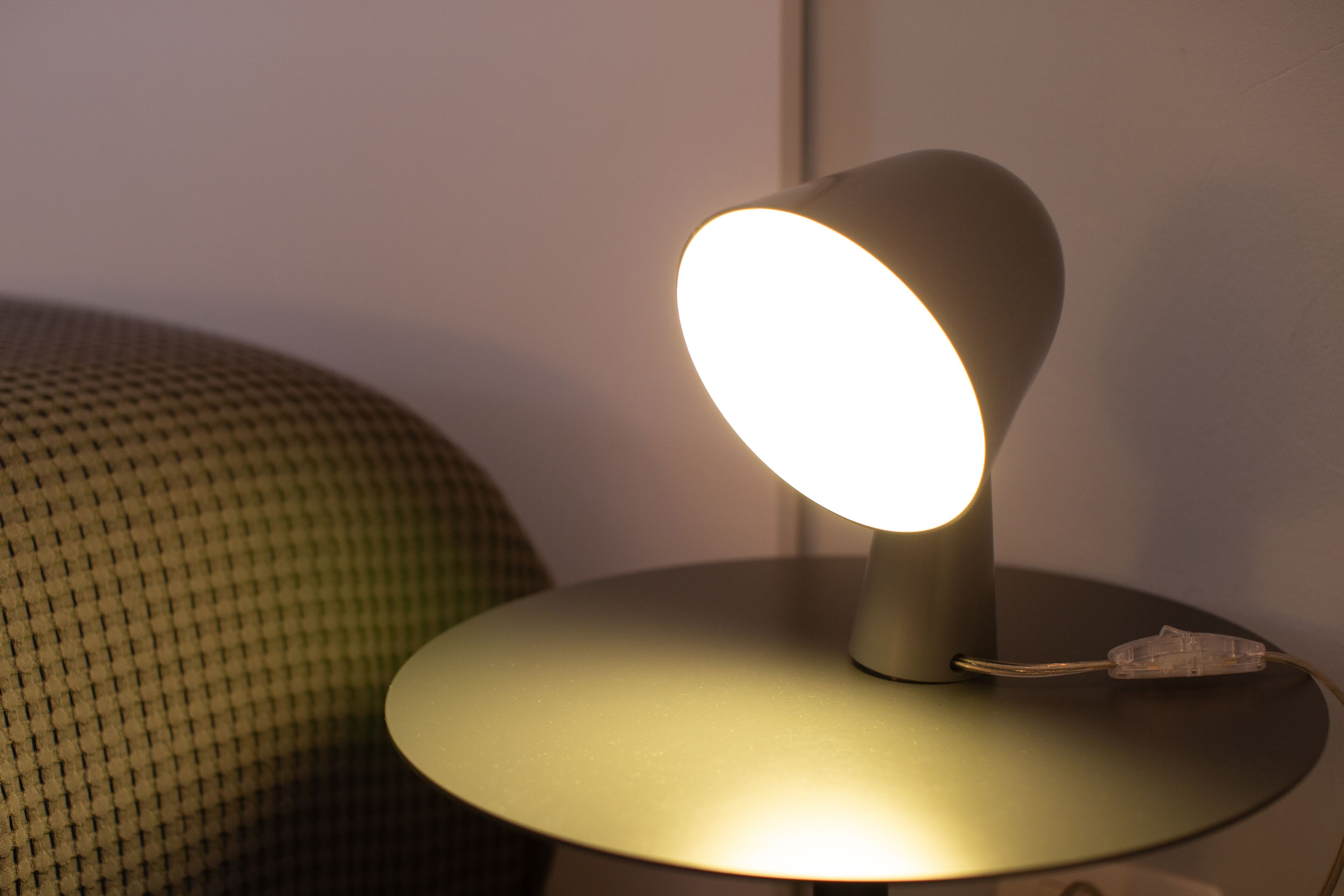 Eine Tischlampe mit runder Basis und kegelförmigem Lampenschirm, auf einem Tisch neben einem strukturierten Stoffstück platziert.