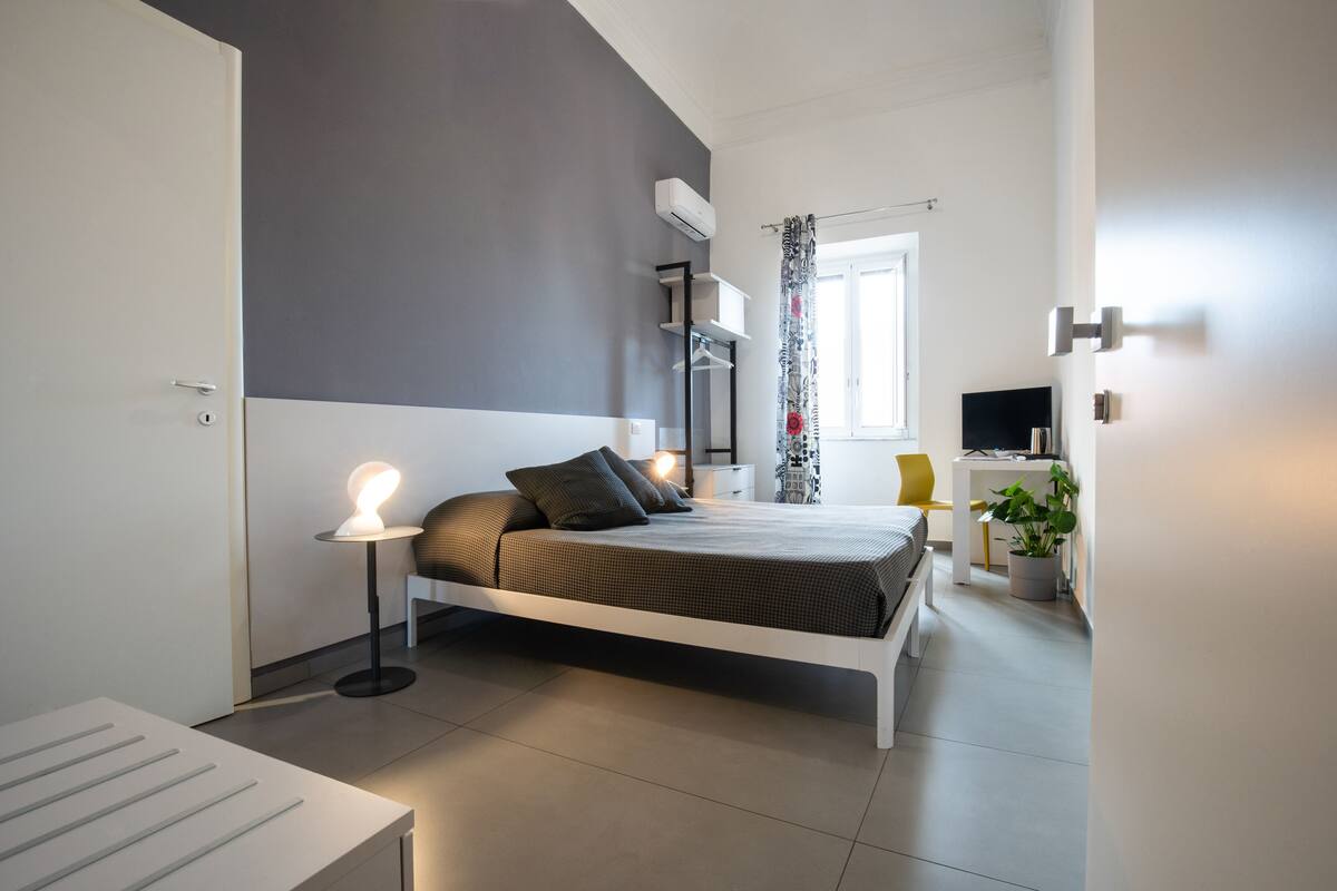 A modern bedroom with a bed, bedside table, lamp, and a desk with a chair.