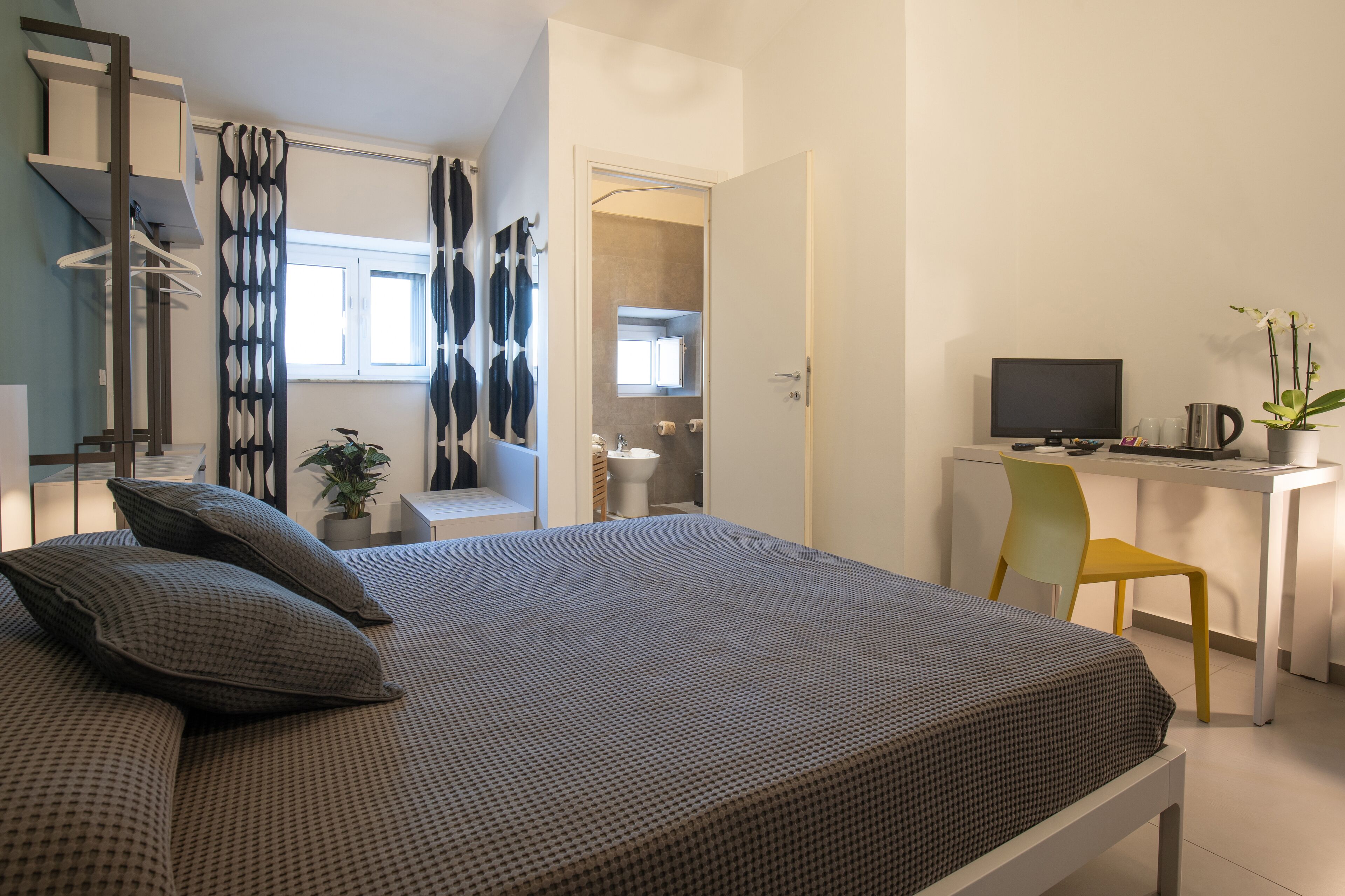 Una camera da letto con un letto, una scrivania, una sedia, una televisione e un bagno visibile attraverso una porta aperta.