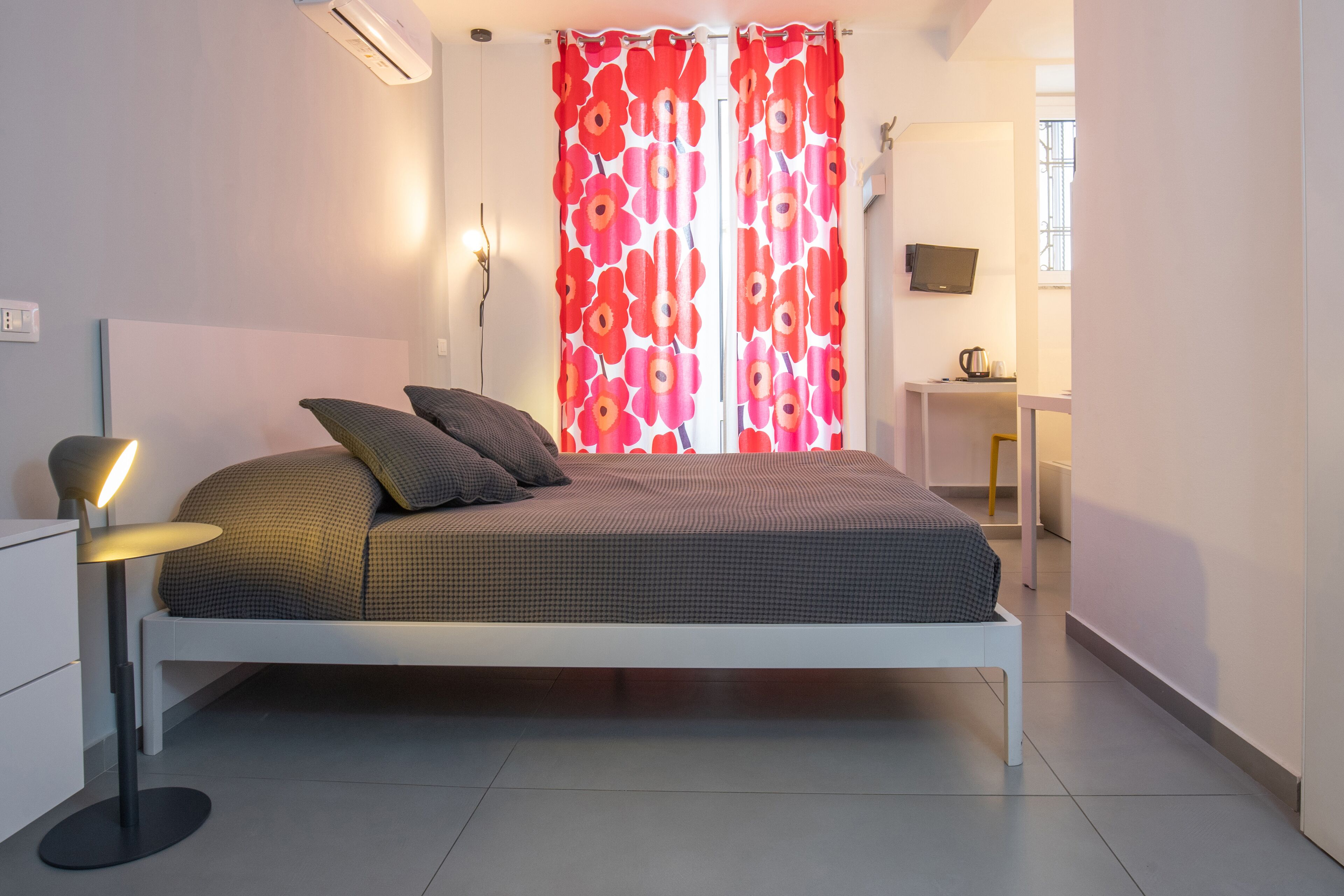 Un dormitorio moderno con cama, almohadas, una lámpara de noche y un escritorio con silla.