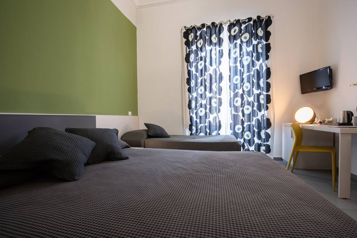 A hotel room with two beds, a desk, a chair, a TV, and a curtain with a circular pattern.
