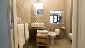 Ein modernes Badezimmer mit Waschbecken, Bidet und Toilette, einem hölzernen Handtuchhalter und einem Spiegel.