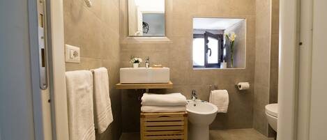 A modern bathroom with a sink, bidet, and toilet, wooden towel rack, and a mirror.