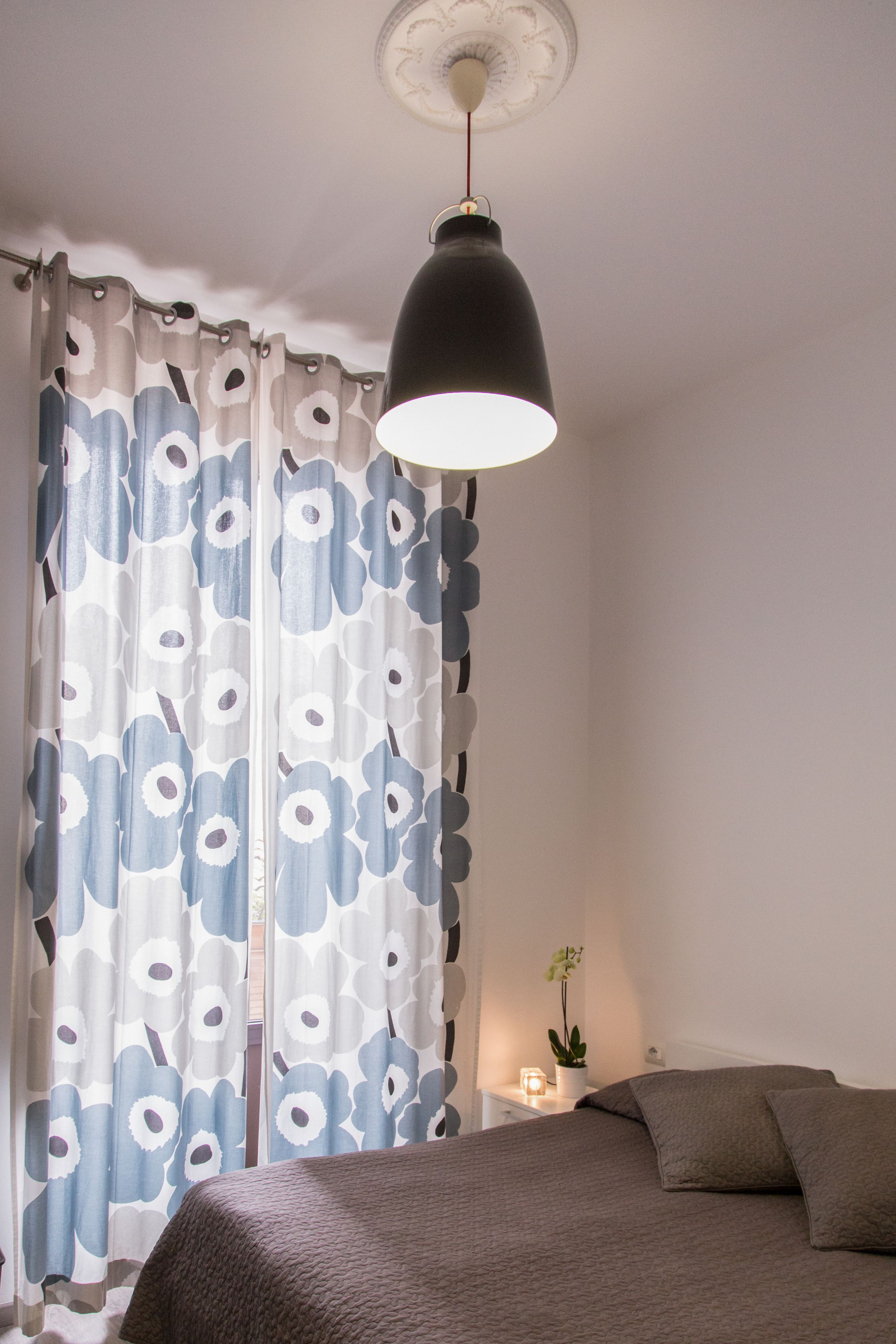 A bedroom with a bed, a nightstand, a lamp, and a window with curtains.