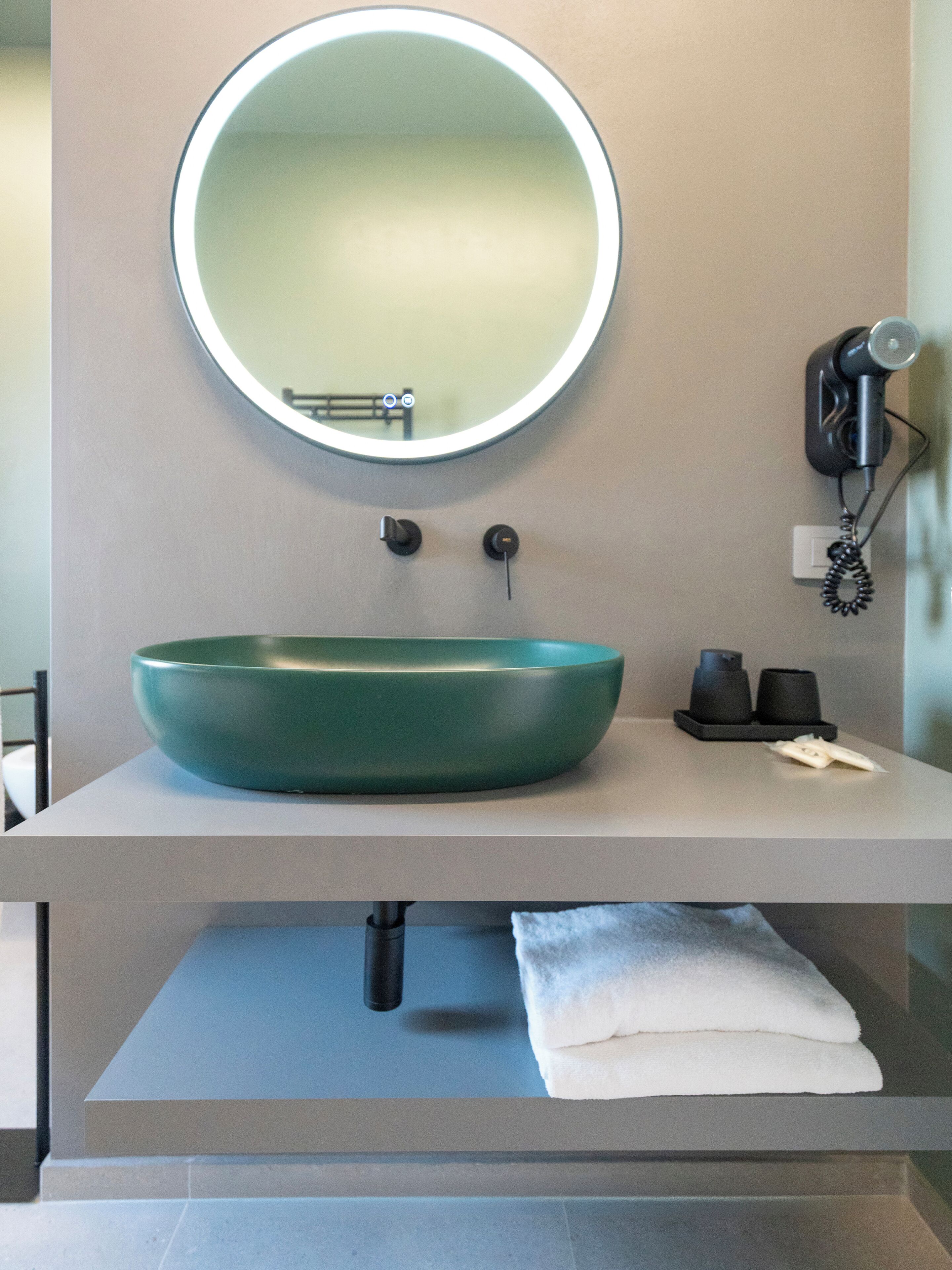 A bathroom with a round mirror, a green sink, a hairdryer, and a towel rack.