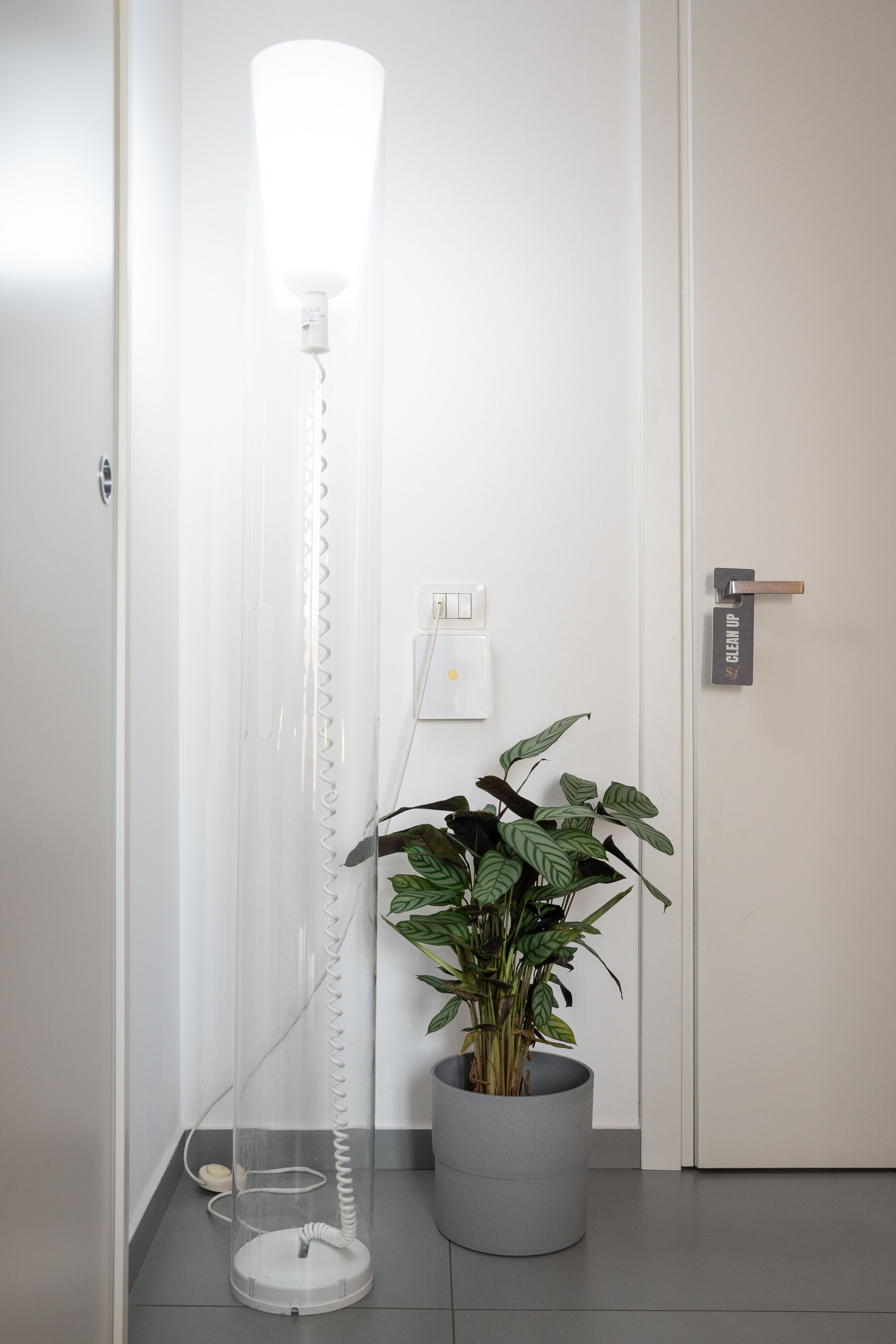 A modern room with a standing lamp, a potted plant, and a door with a 'CLEANUP' sign.