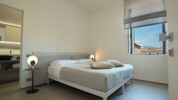 Camera da letto moderna con un letto, lampade da comodino, una finestra con vista e un bagno con lavandino e specchio.