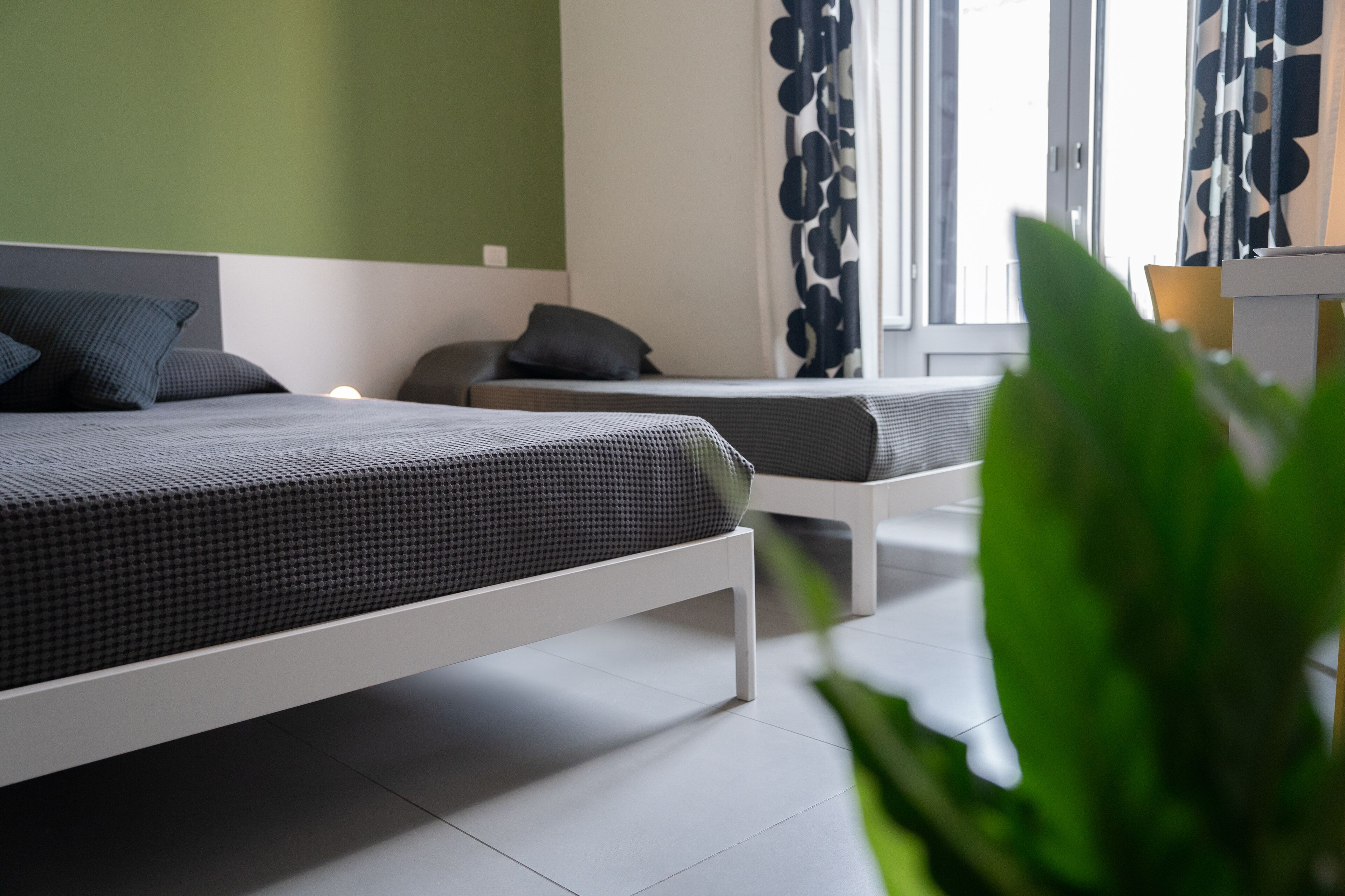 A modern bedroom with two beds, a green wall, and a large window with curtains.