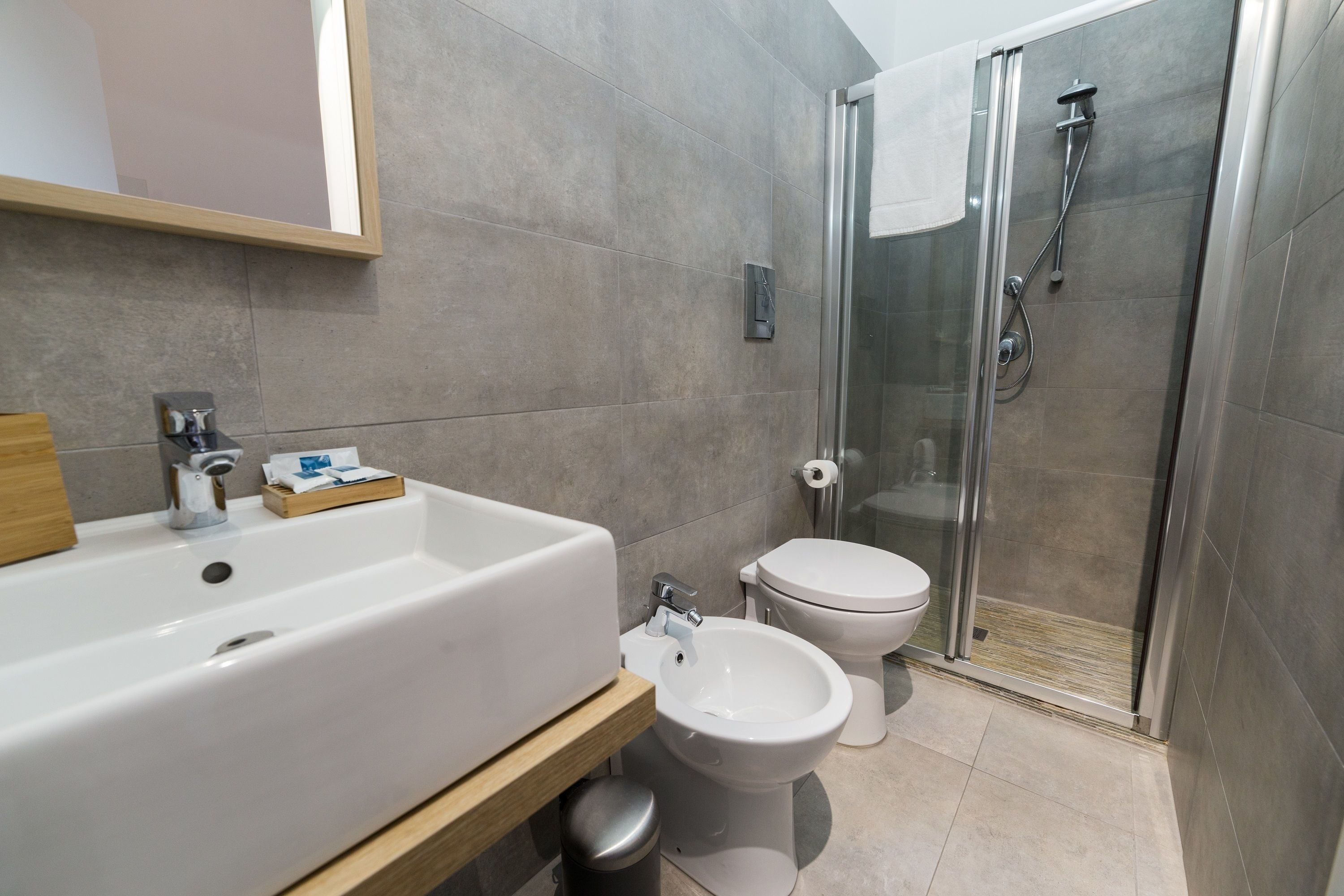 A modern bathroom with a large white sink, a bidet, and a glass-enclosed shower.