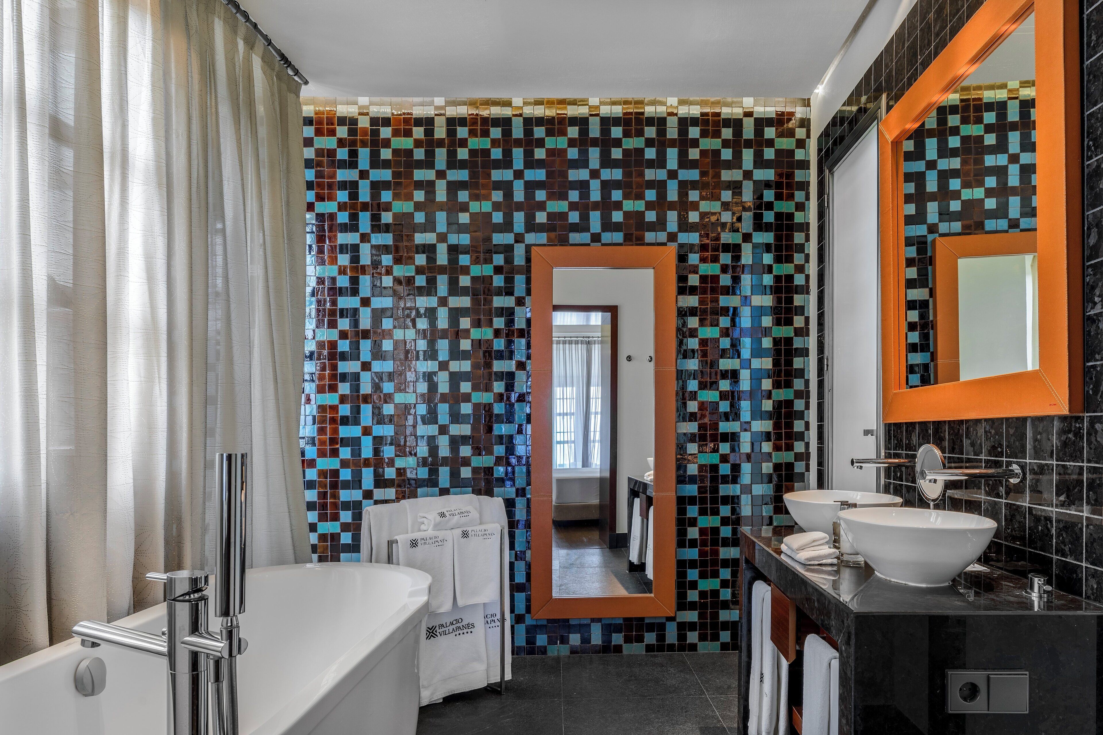 Un baño moderno con pared de mosaicos, un espejo grande, una bañera y dos lavamanos.