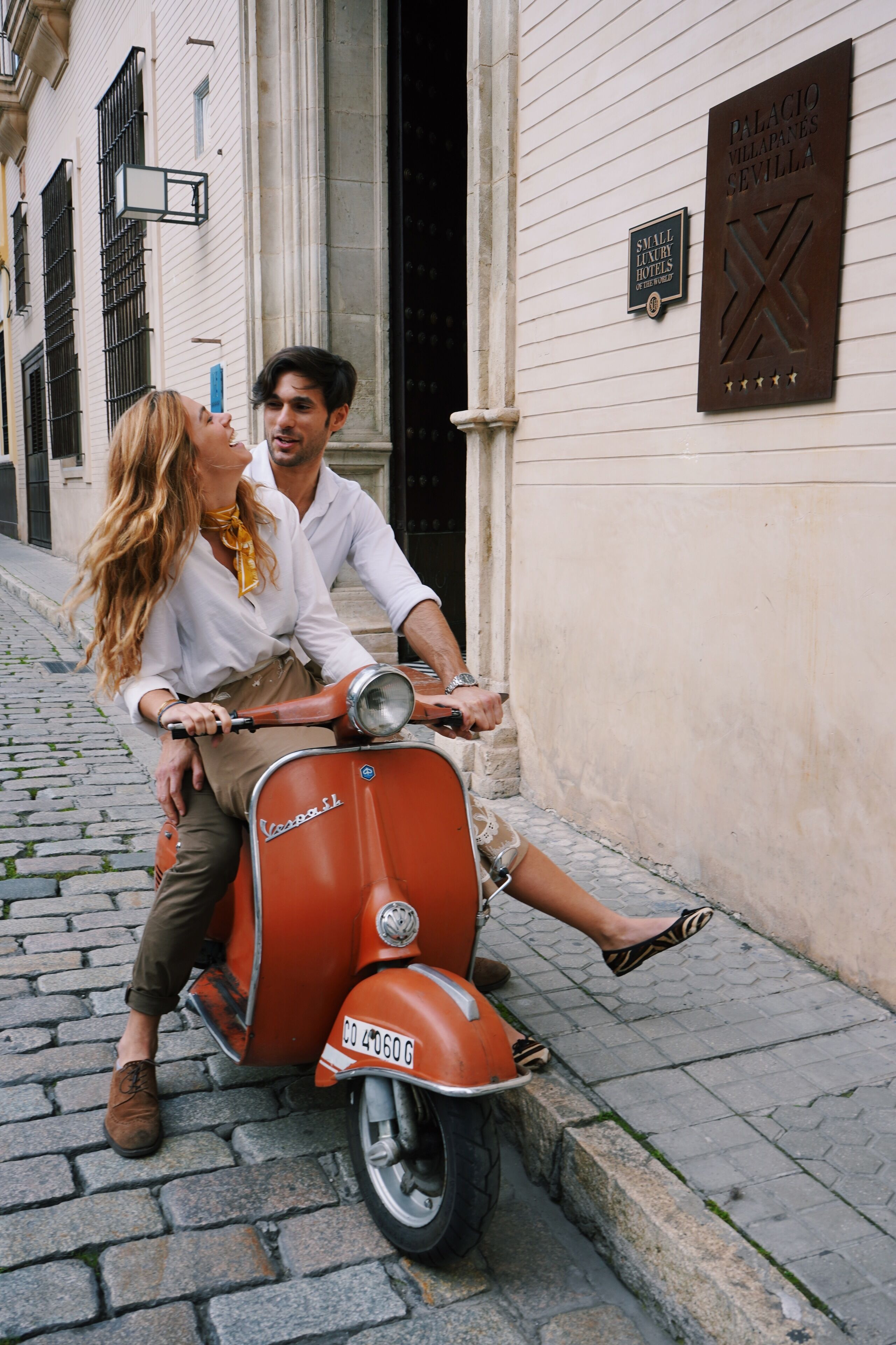 A couple on a vintage Vespa scooter parked on a cobblestone street.