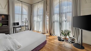 A hotel room with a large bed, a desk with a computer, a TV, and a dining area with a table set for two. - CoolRooms Palacio Villapanés 5 GL (Seville)