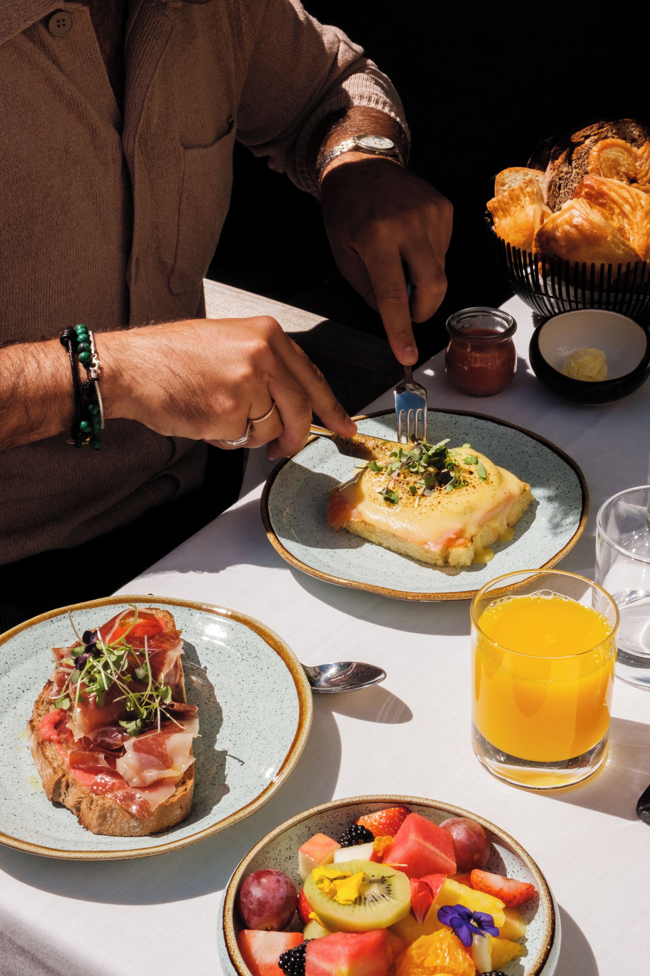 Una mesa con un plato de comida, un vaso de jugo de naranja y una cesta de pan.