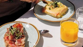 Una mesa con un plato de comida, un vaso de jugo de naranja y una cesta de pan.