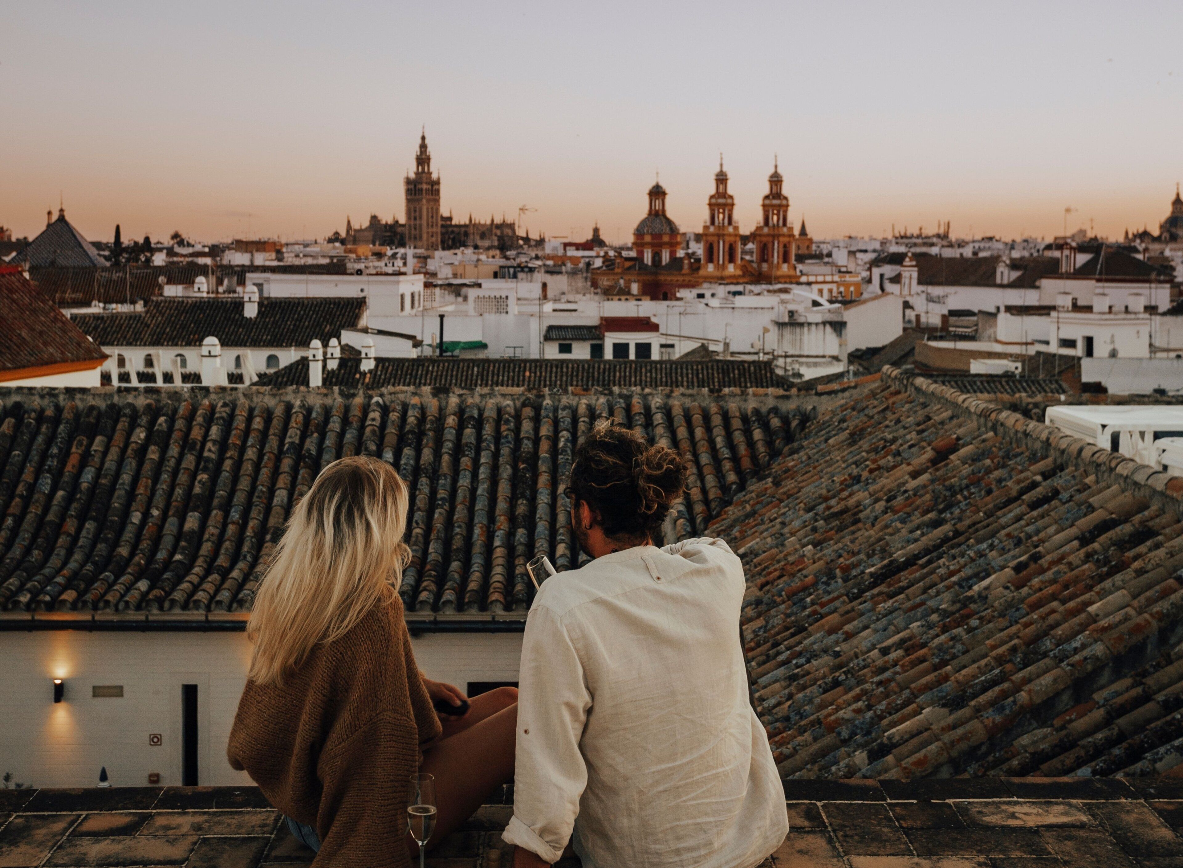 Two people sitting on a rooftop terrace overlooking a cityscape with historical buildings.