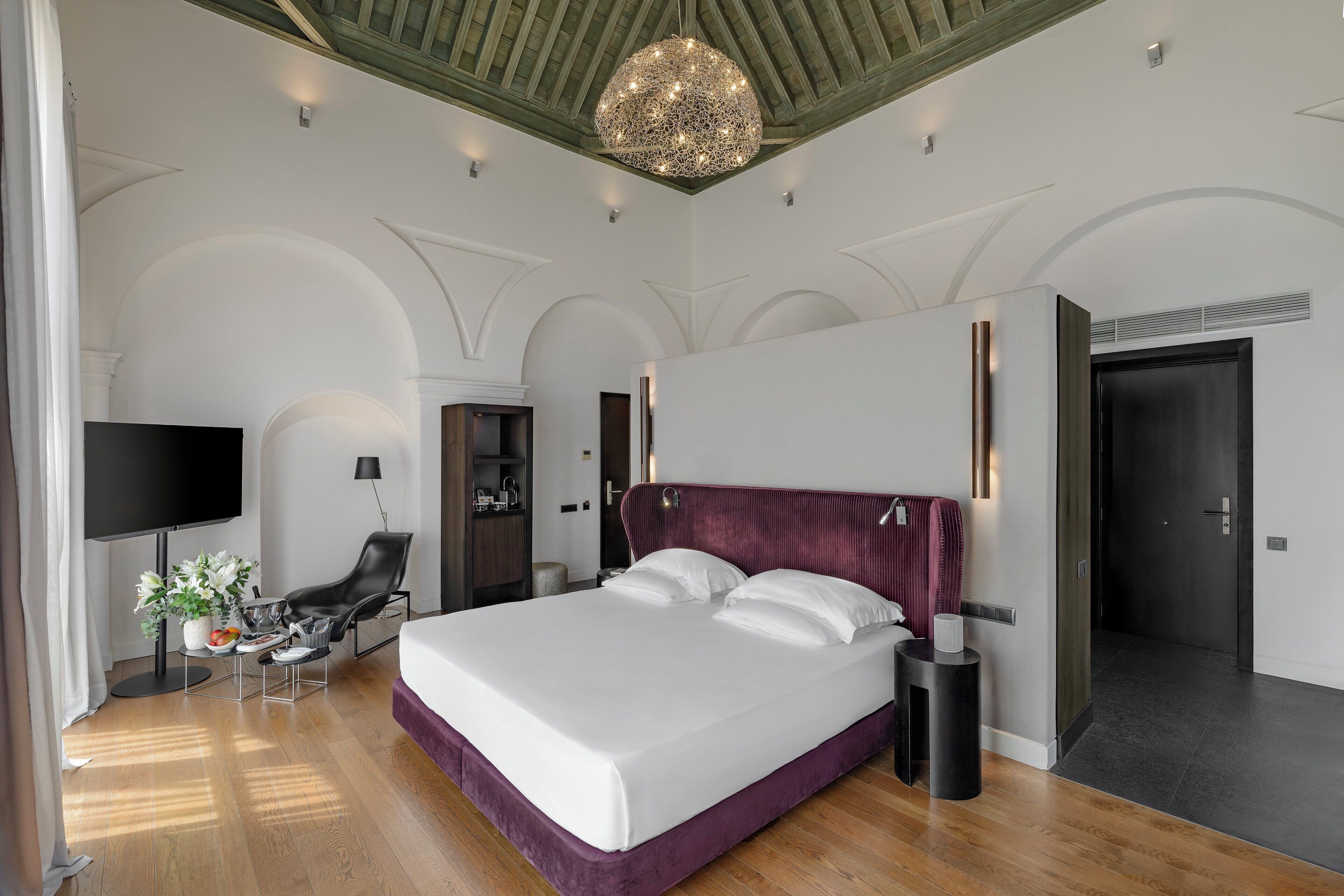 Une chambre d’hôtel moderne dotée d’un grand lit, d’une télévision, d’un coin salon et d’un lustre.