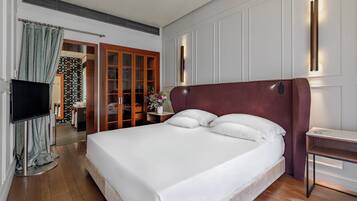Una habitación de hotel moderna con una cama grande, un televisor, un escritorio y un baño visible a través de una puerta abierta.