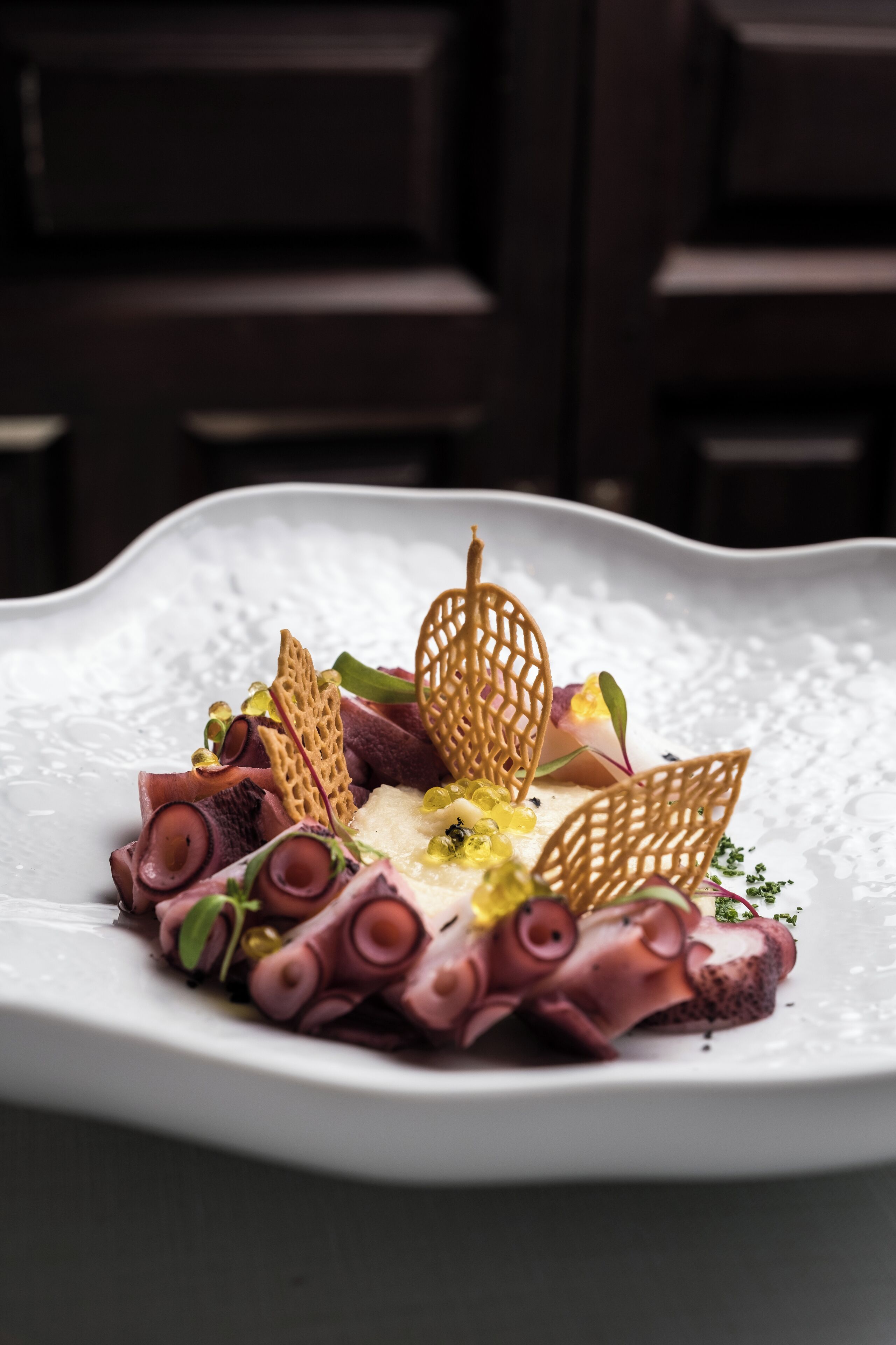 Une assiette blanche contenant des rouleaux de viande, des feuilles décoratives et une garniture jaune.