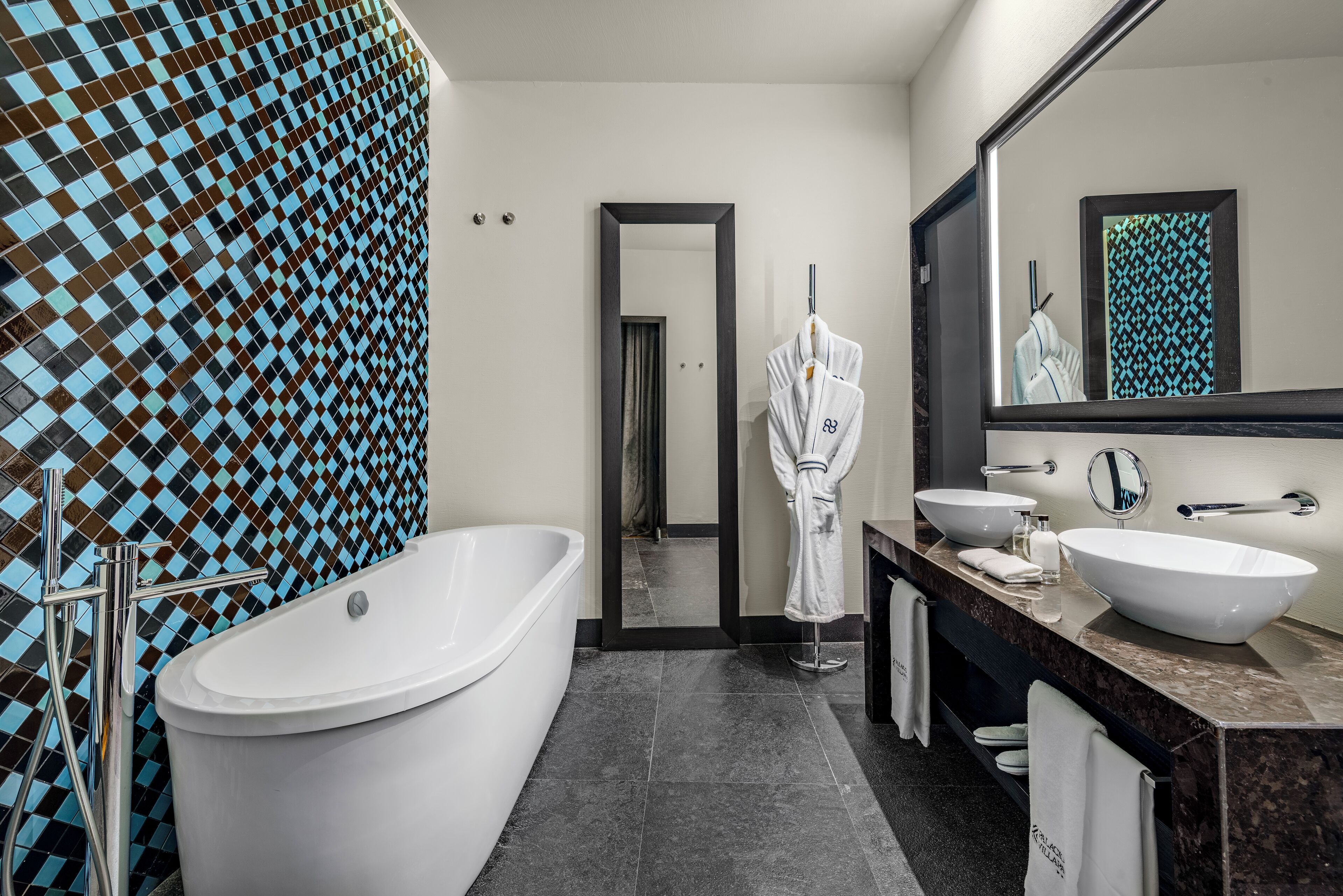 Un baño moderno con una bañera grande, dos lavamanos, un espejo y un revestimiento de pared estampado.