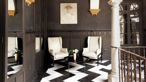 A hallway with a checkered floor, two white armchairs, a small table with a vase, and a framed picture on the wall. - CoolRooms Palacio Villapanés 5 GL (Seville)