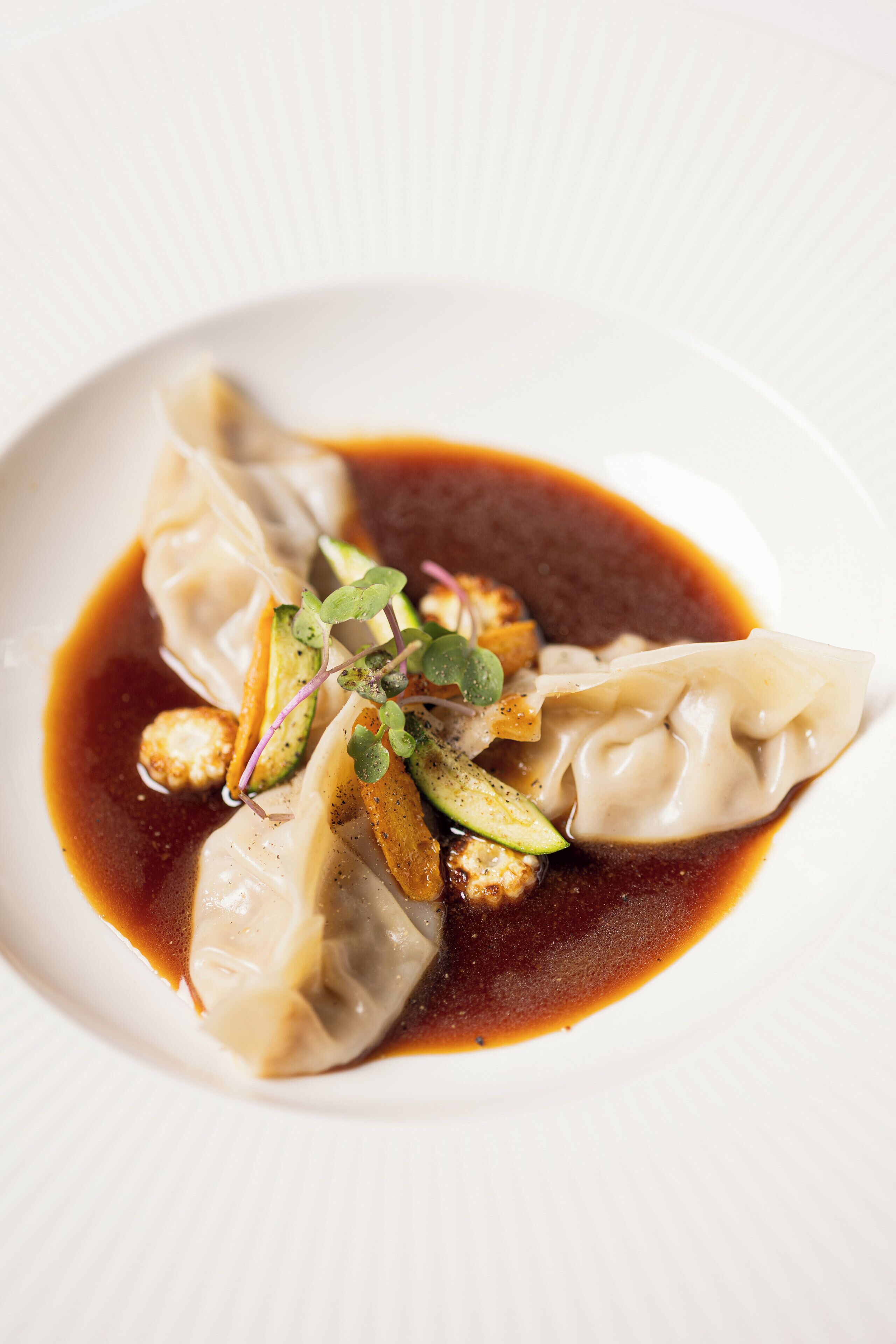 A plate of dumplings with a dark sauce and garnishes.