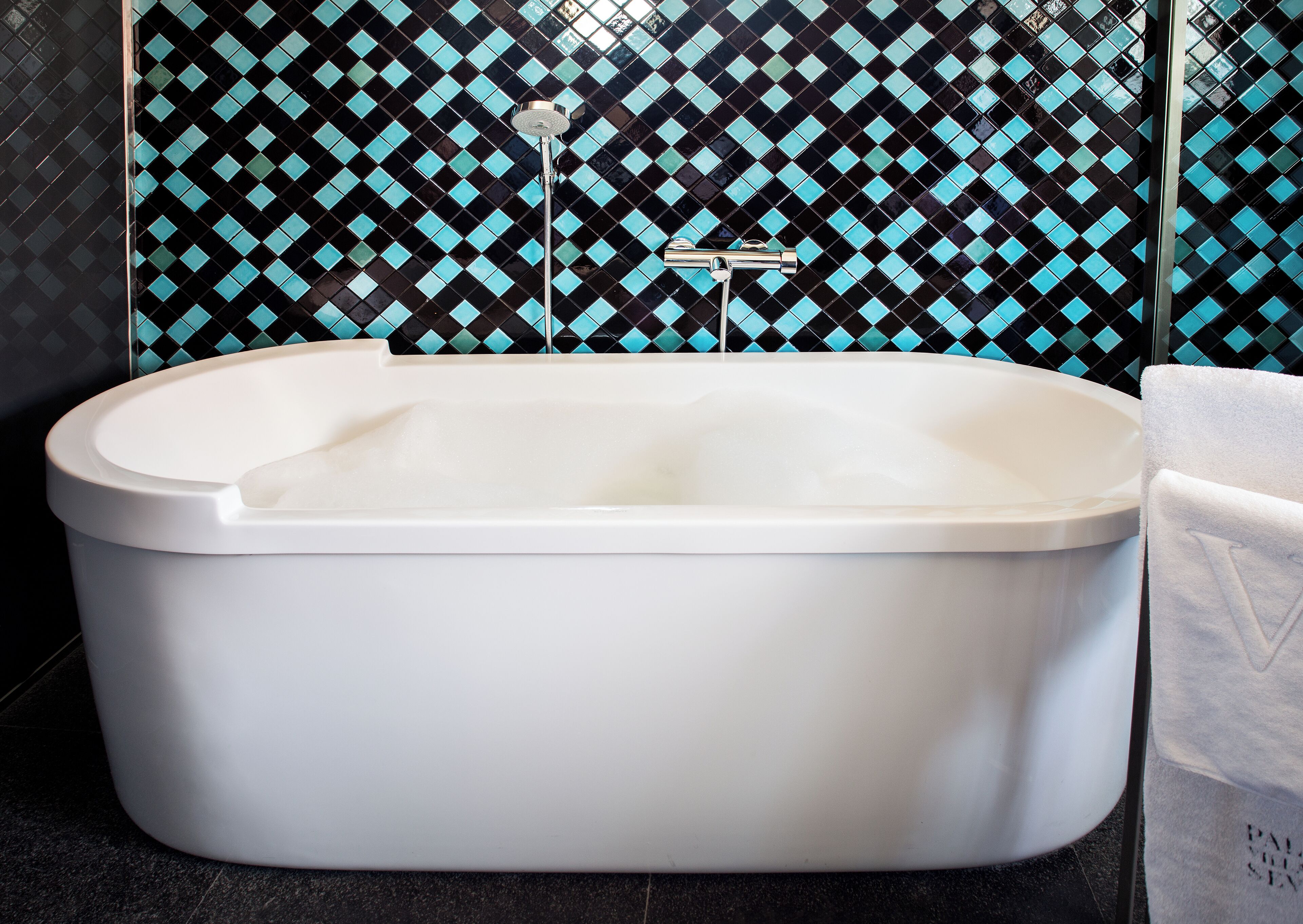 A modern bathroom with a freestanding bathtub, a visible showerhead, and a tiled wall with a diamond pattern.